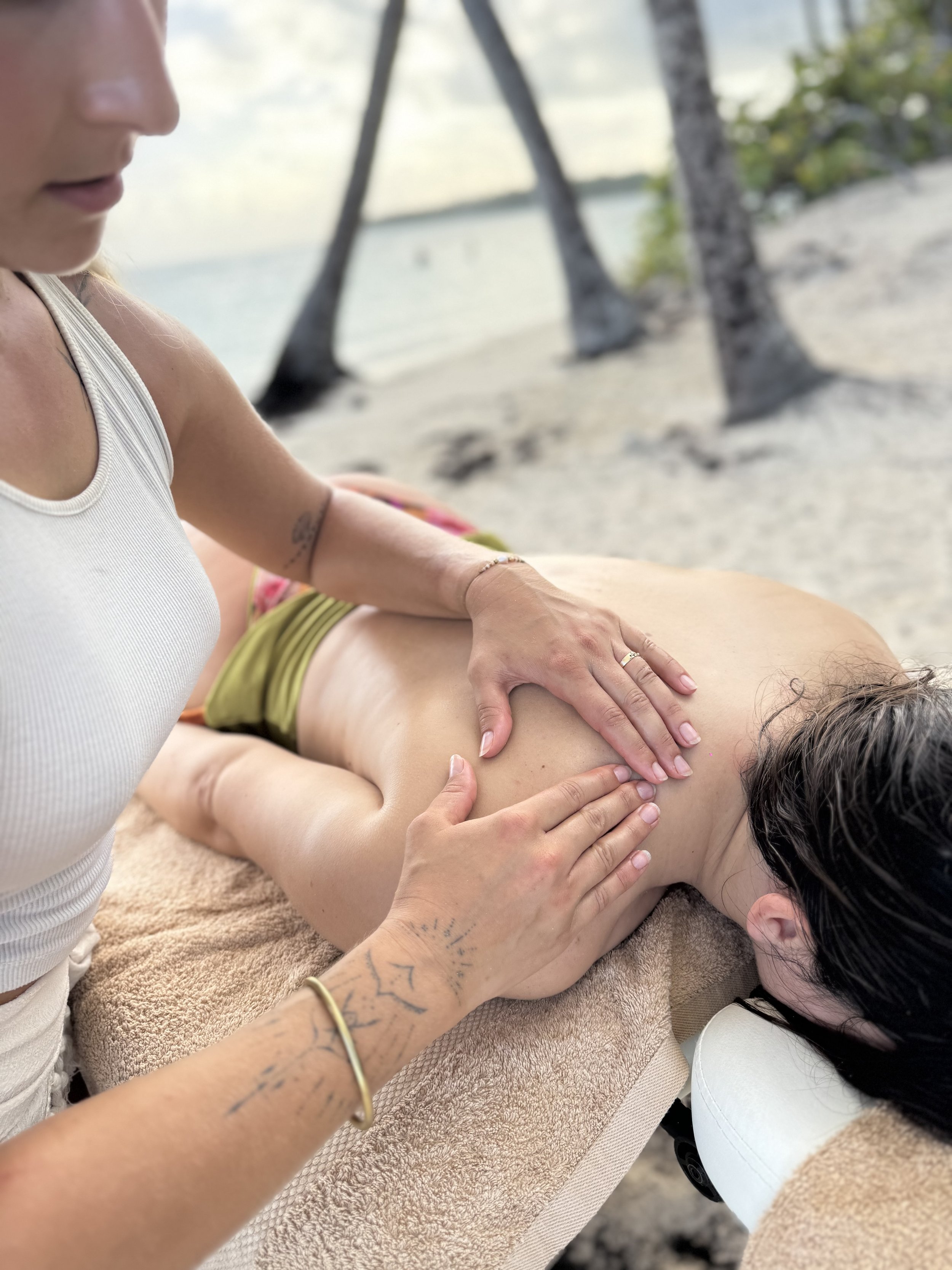 Une personne donne un massage ou une séance de relaxation à une autre personne allongée sur un lit ou une table, avec un décor de plage ou de nature en arrière-plan.