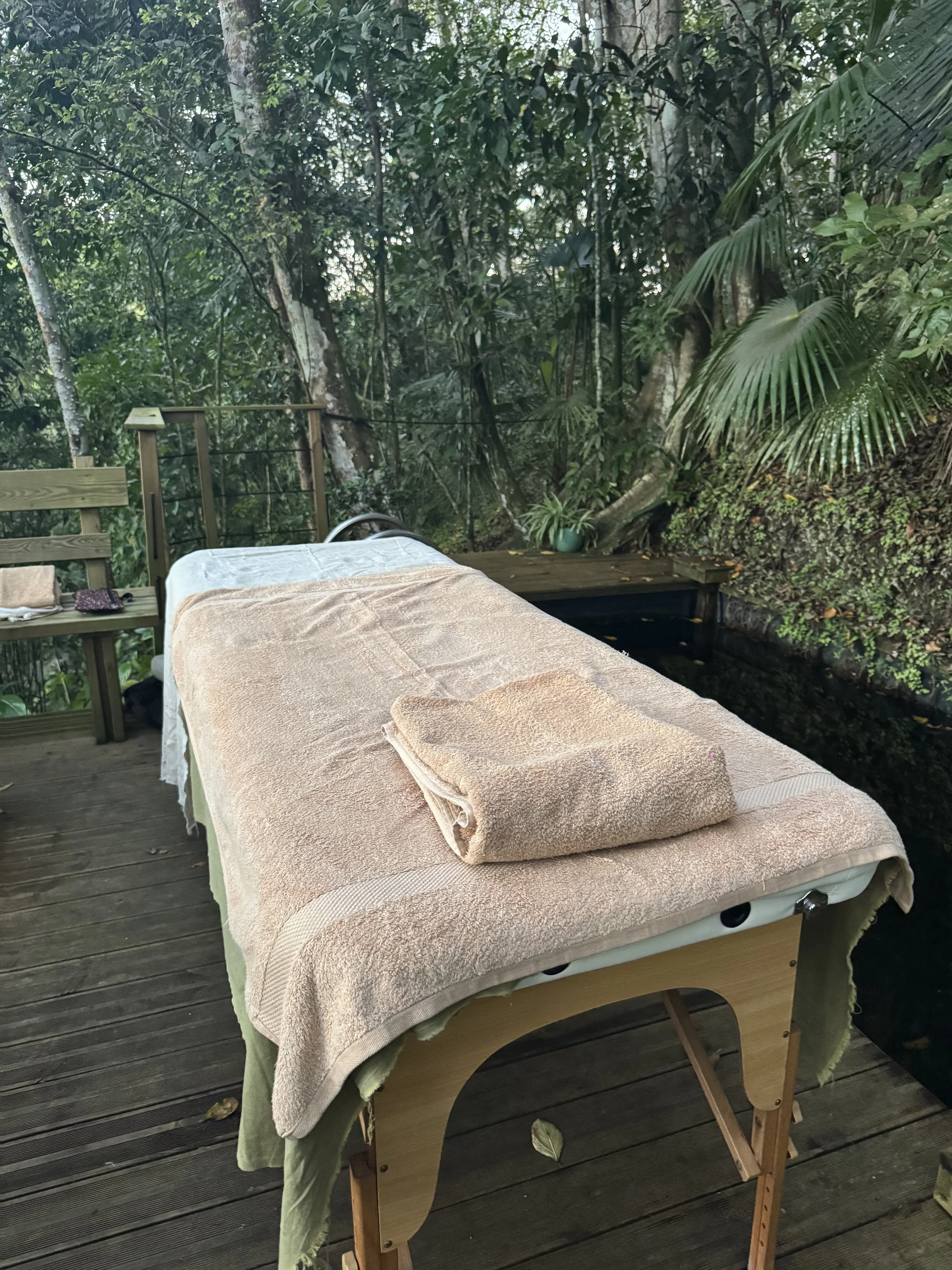 Massage de spa ou massothérapie en plein air sur une table avec un drap beige, dans un environnement forestier dense avec beaucoup de végétation.
