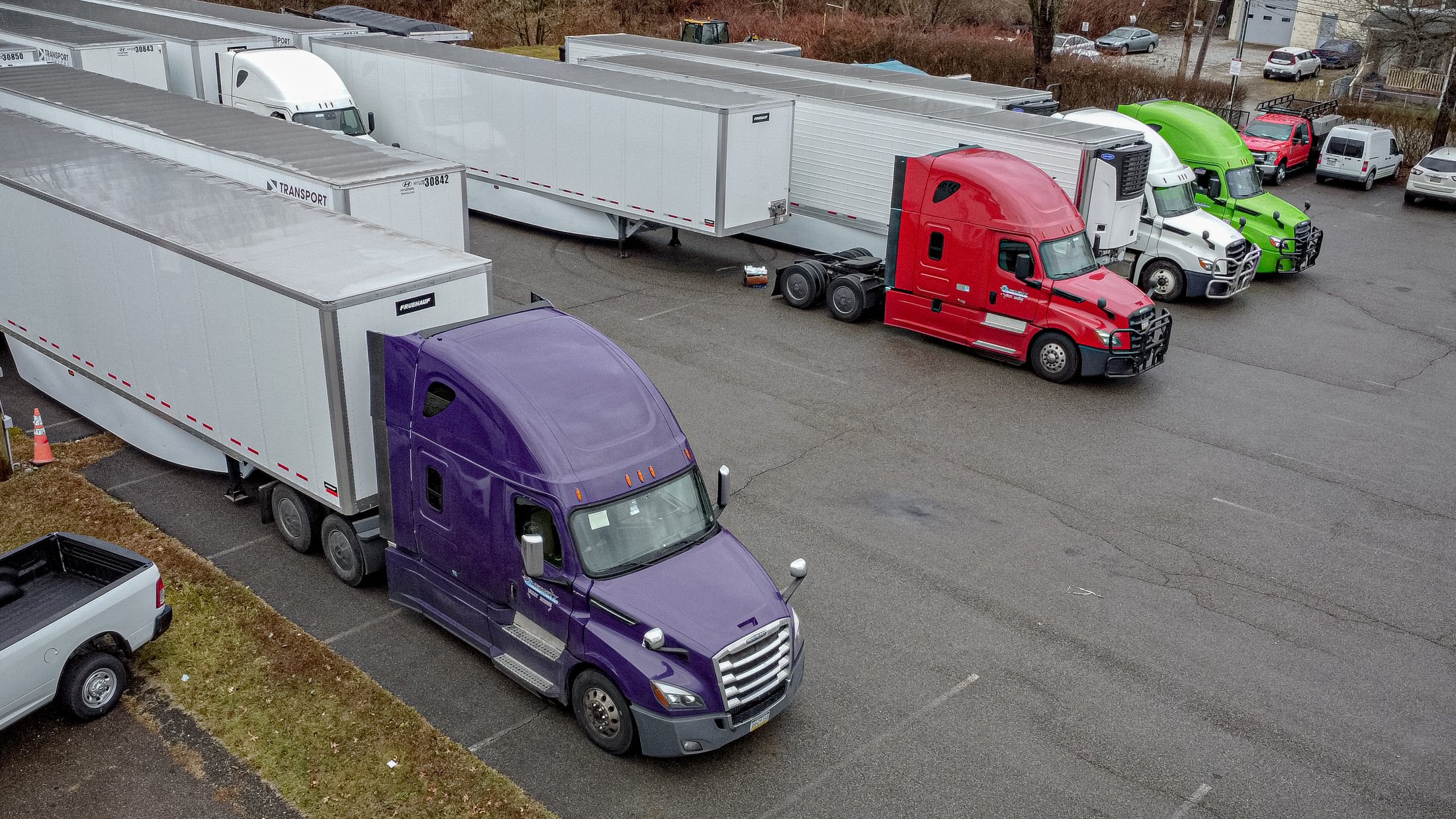 Colorful semi-trucks parked in a lot, including purple, red, and green trucks with attached trailers.
