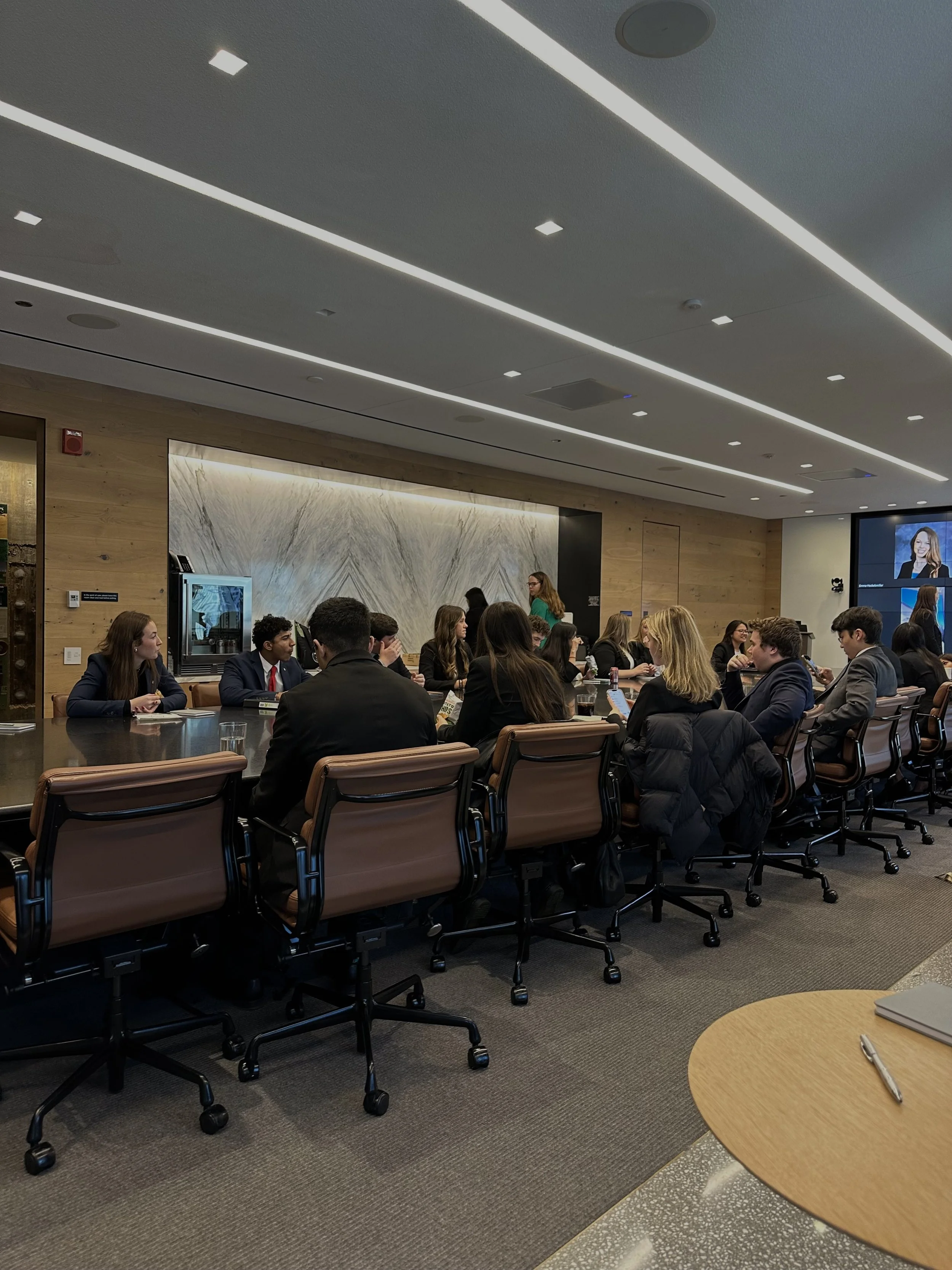 Business meeting or conference with people seated around a large table in a modern office or conference room.