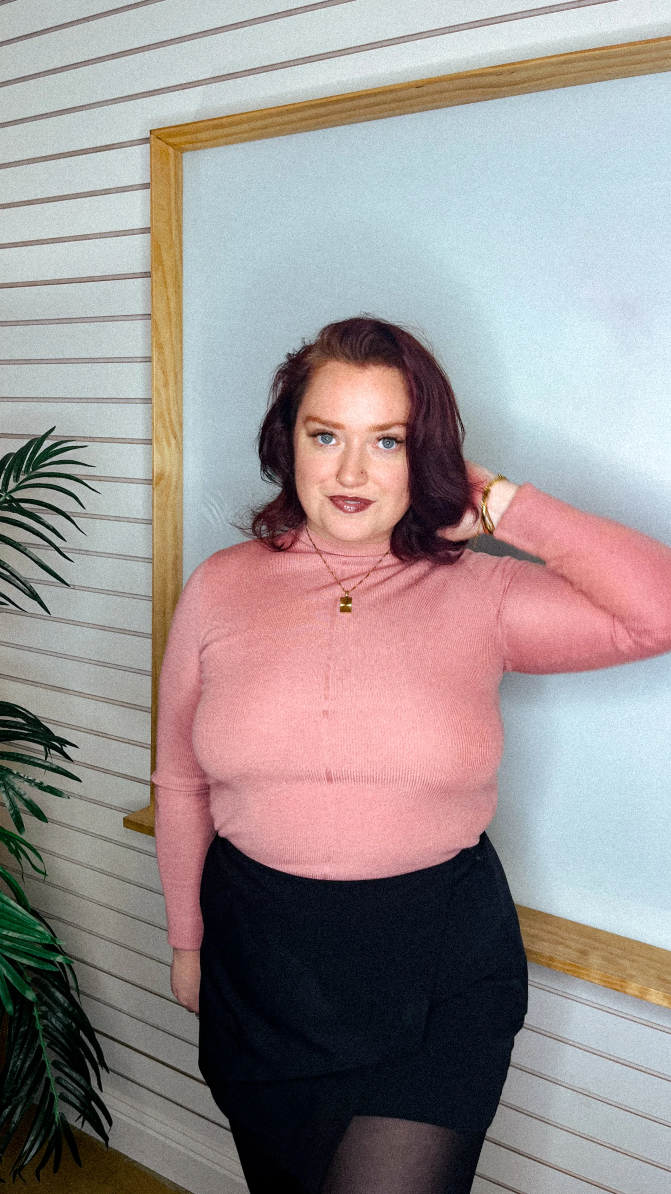 Meaghan, the Hot Girl CFO, standing in front of a white board. She's wearing a pink sweater and a black skirt. She has her hand behind her head and is looking directly into the camera.