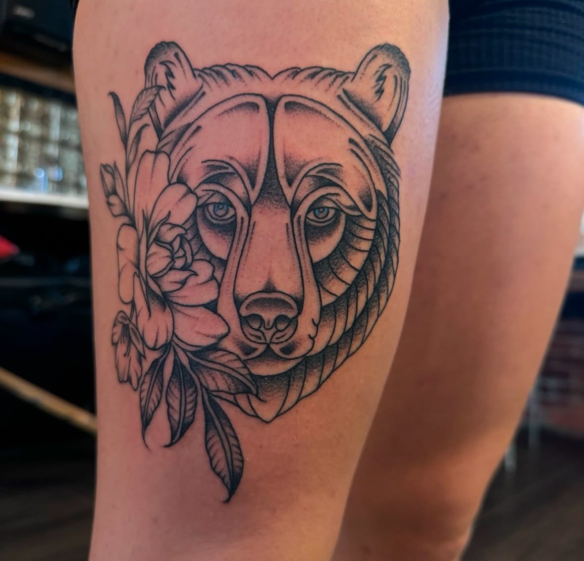 Tattoo of a bear's face with flowers on a person's leg