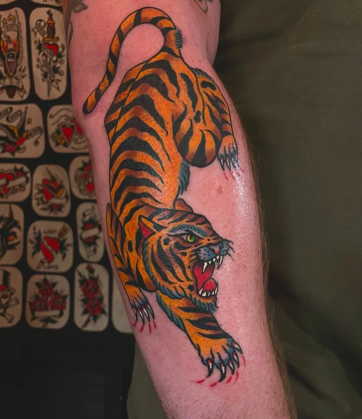 A colorful tiger tattoo on a person's arm with flash art designs in the background.
