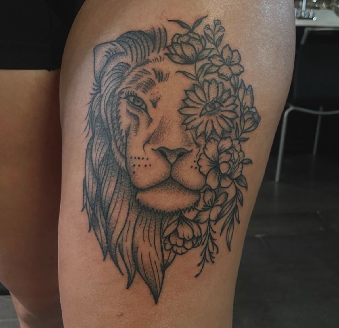 Tattoo of a lion with floral elements on leg