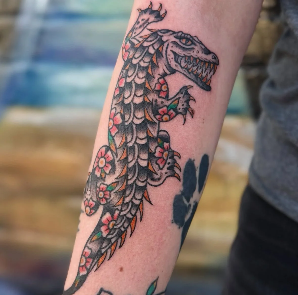 Tattoo of a stylized alligator with floral patterns on a person's forearm.