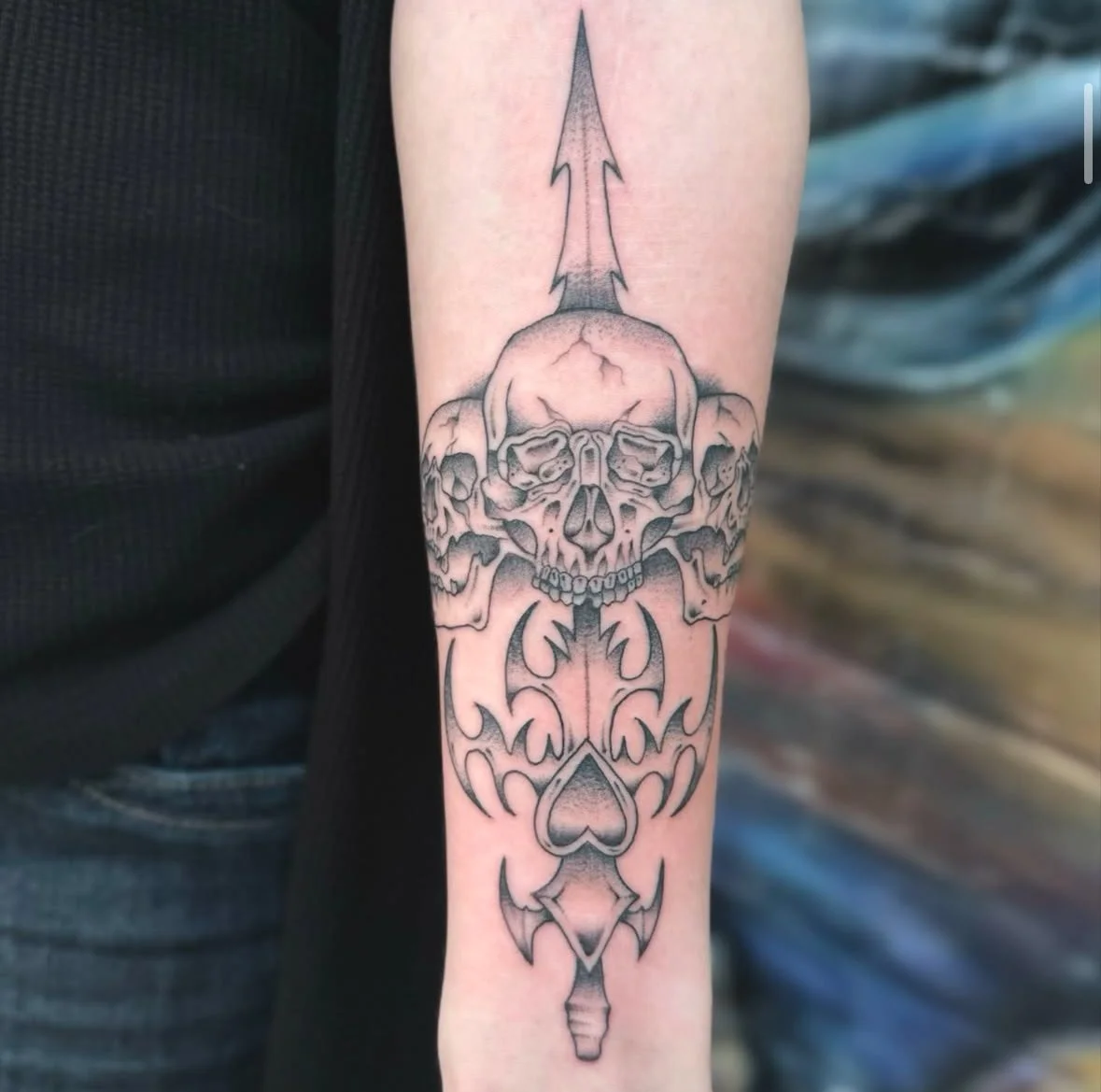 Tattoo of a skull with arrow and tribal designs on forearm