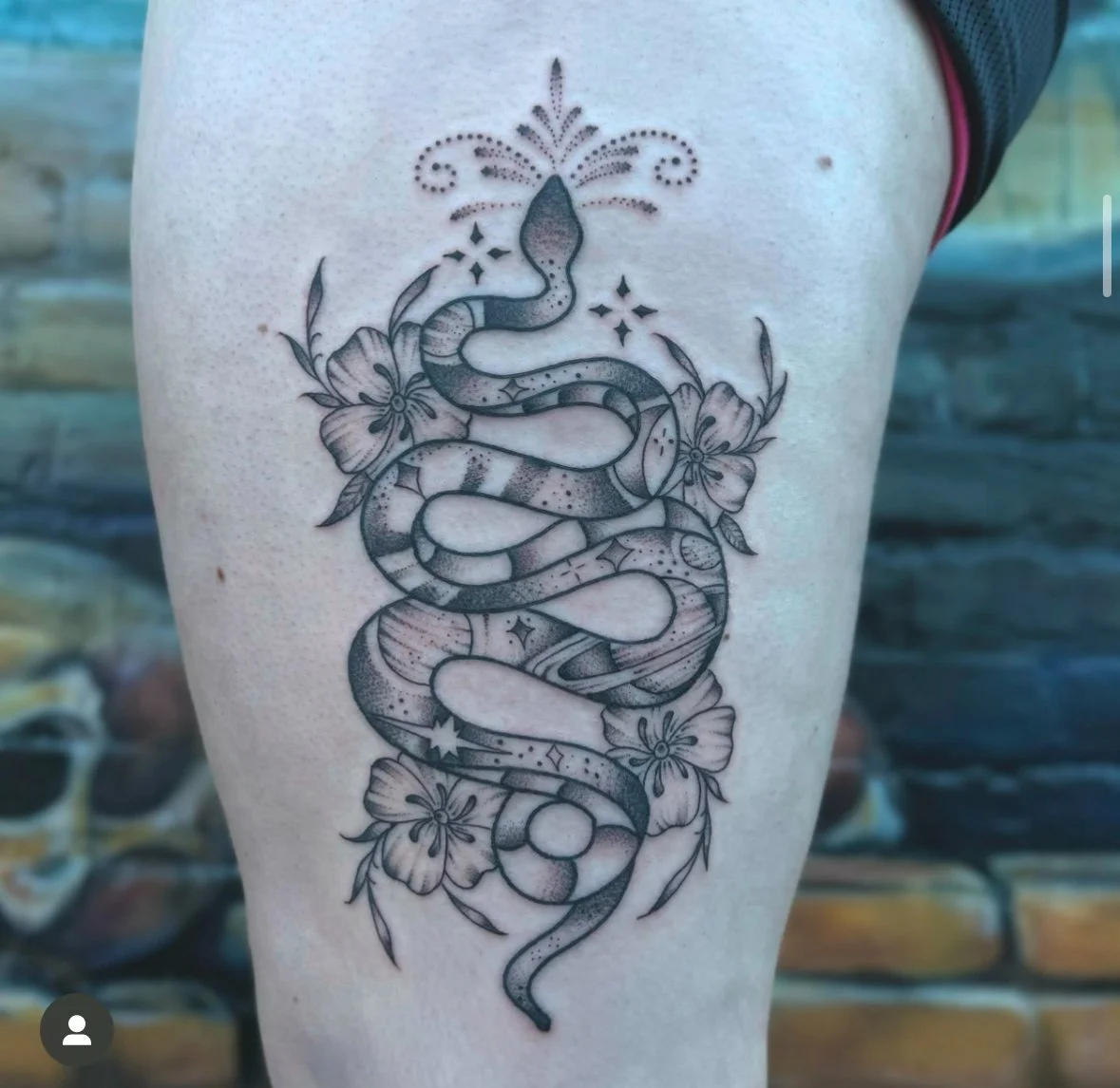 Tattoo of a snake with floral elements and decorative symbols on a person's thigh.