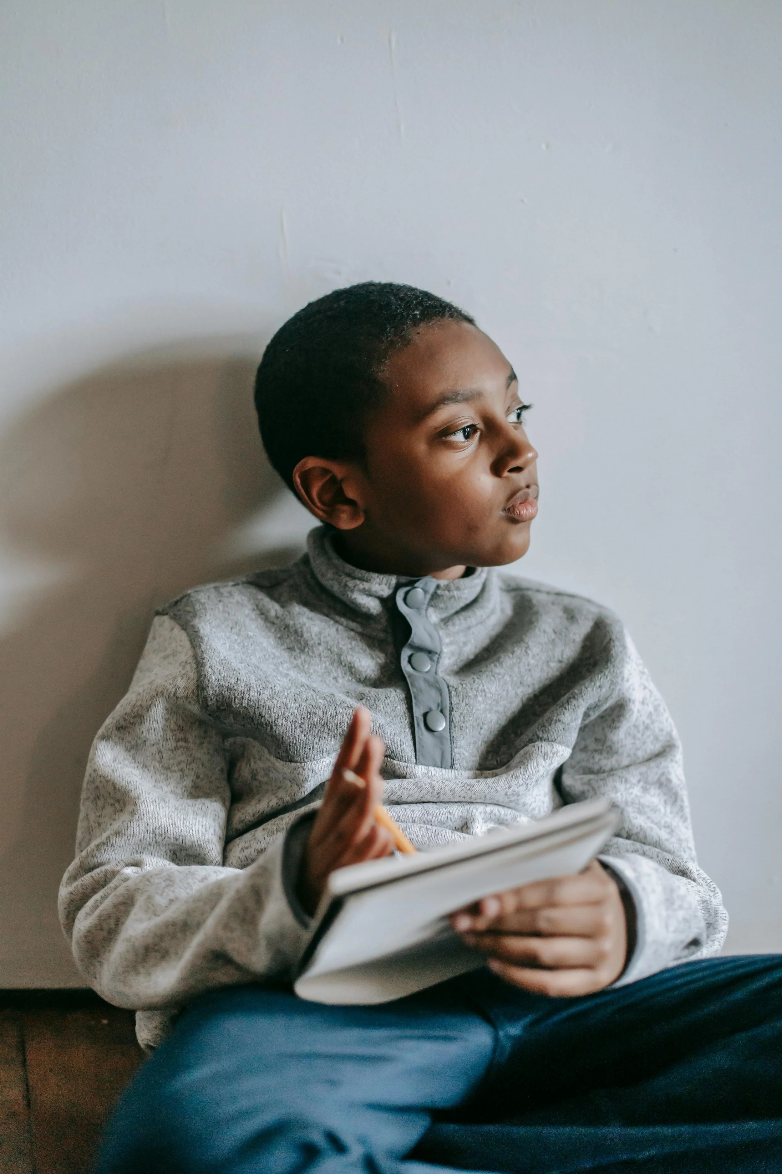 A child looks pensively to the side while writing in a notebook