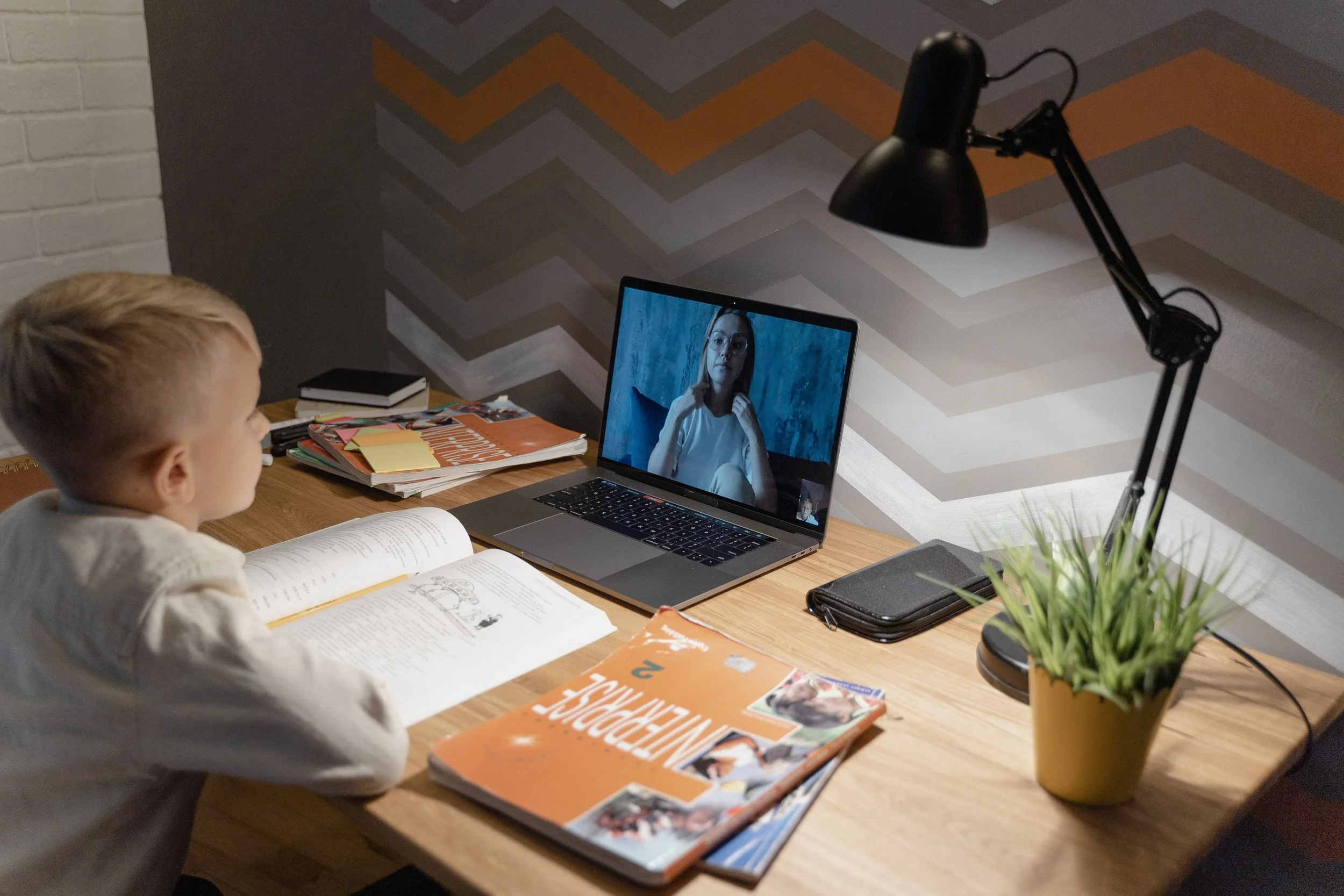 A student sits at an organized desk while in a virtual one on one meeting with his teacher