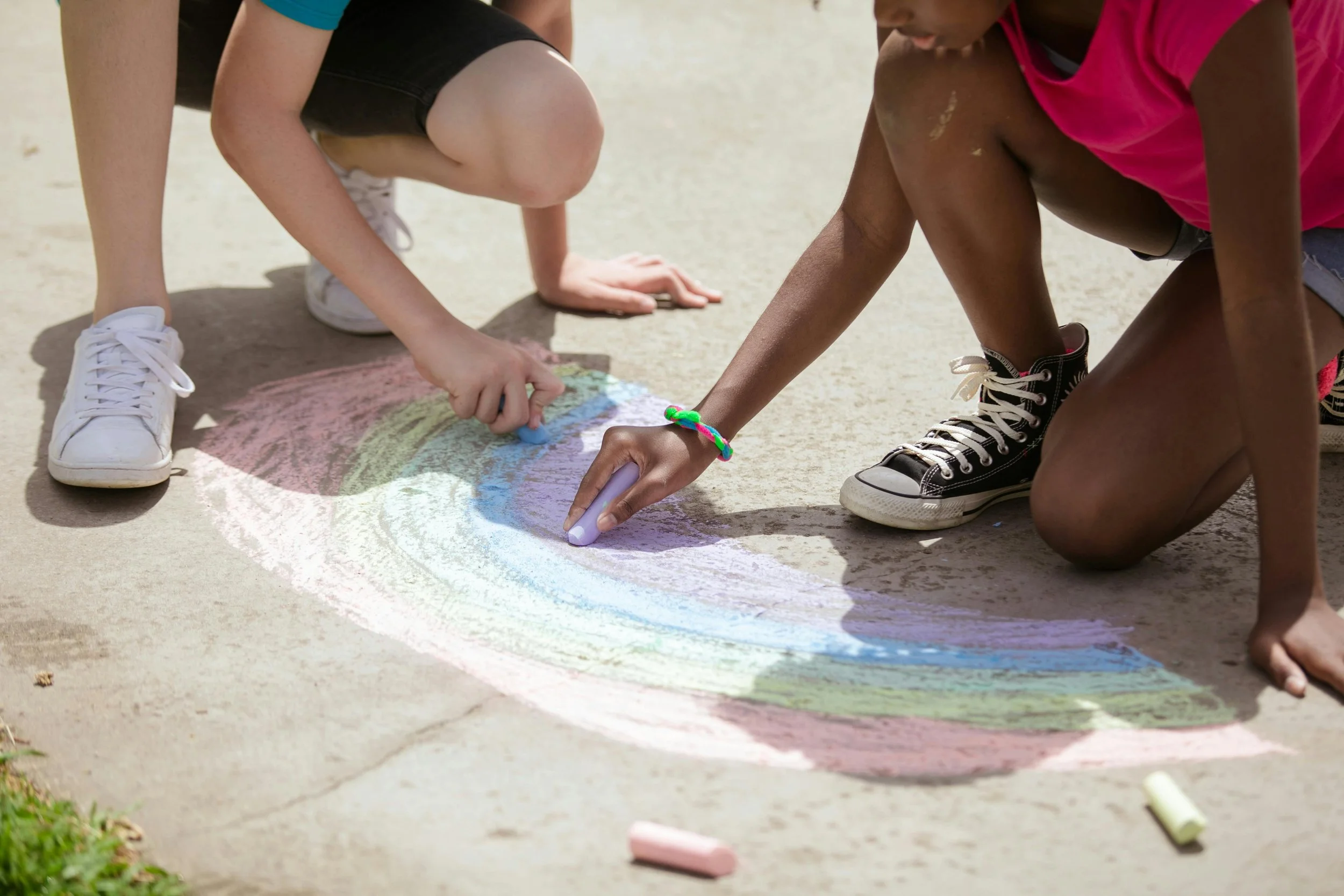 Two children draw a rainbow with sidewalk chalk