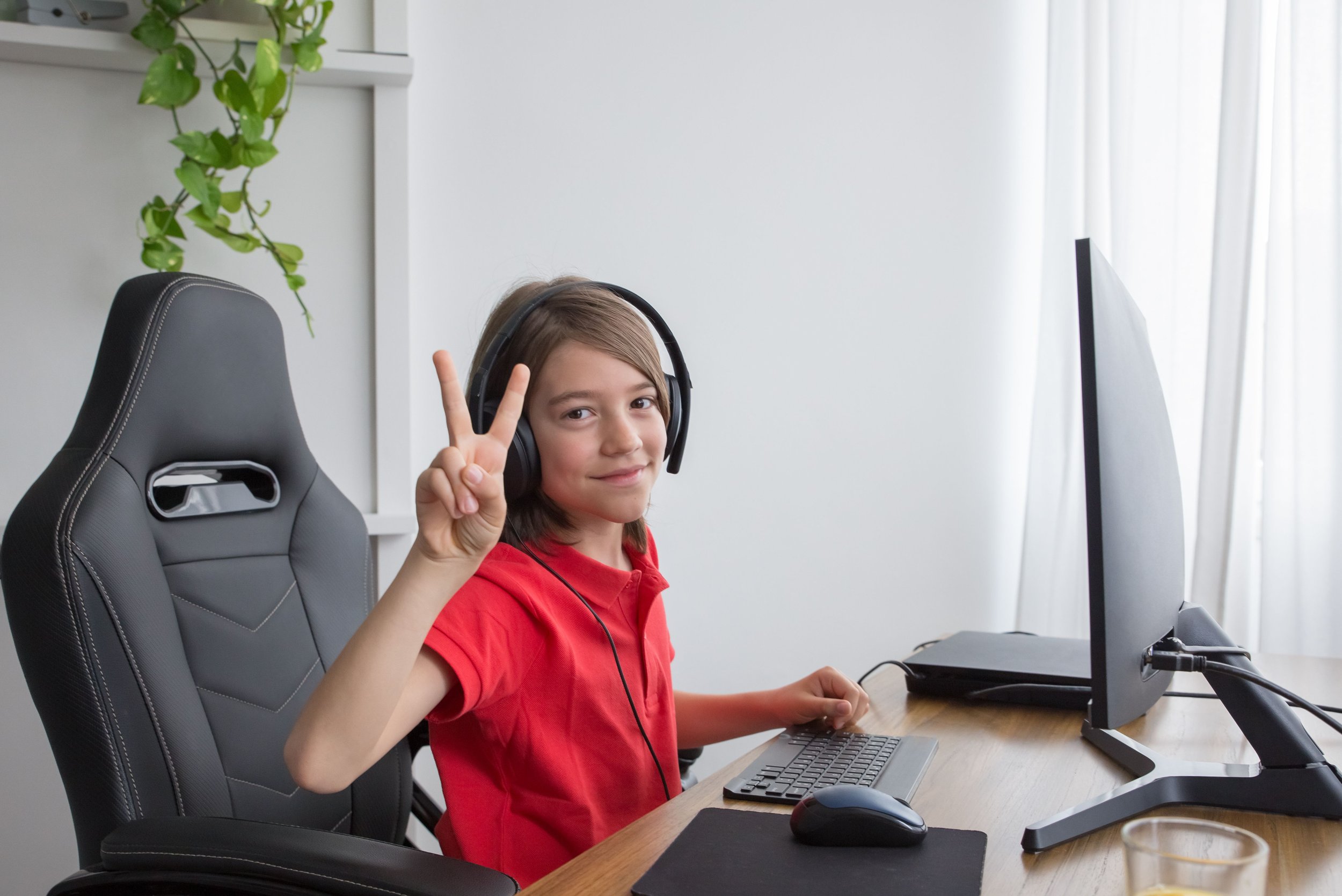 A virtual student sits at a desk and holds up a peace sign