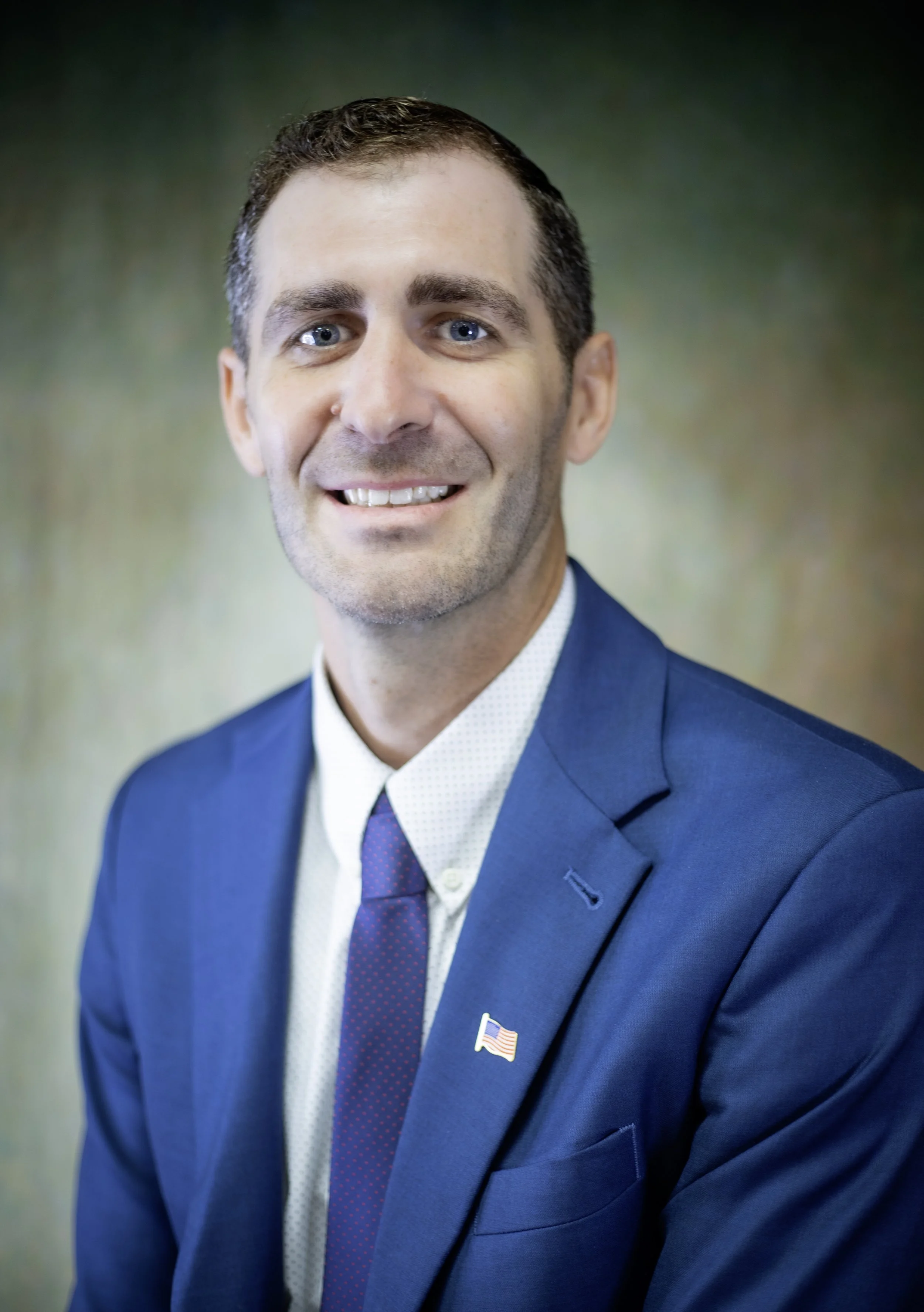 Man in blue suit with flag lapel pin smiling, Jordan Brewer