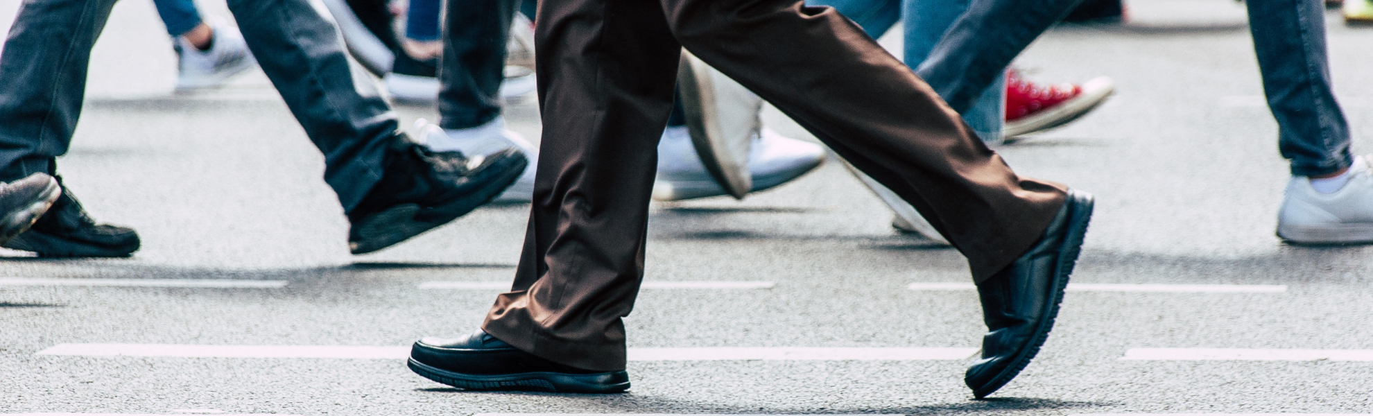 Close-up of pedestrians' legs crossing a street, focused on brown trousers and black shoes mid-stride.