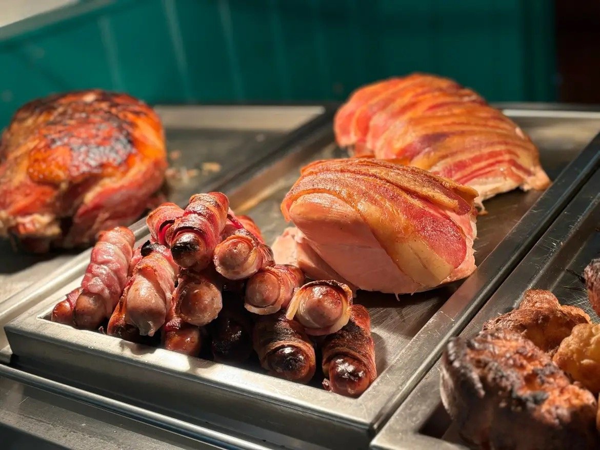 Assorted cooked meats on a tray, including bacon-wrapped sausages and bacon-wrapped pork.