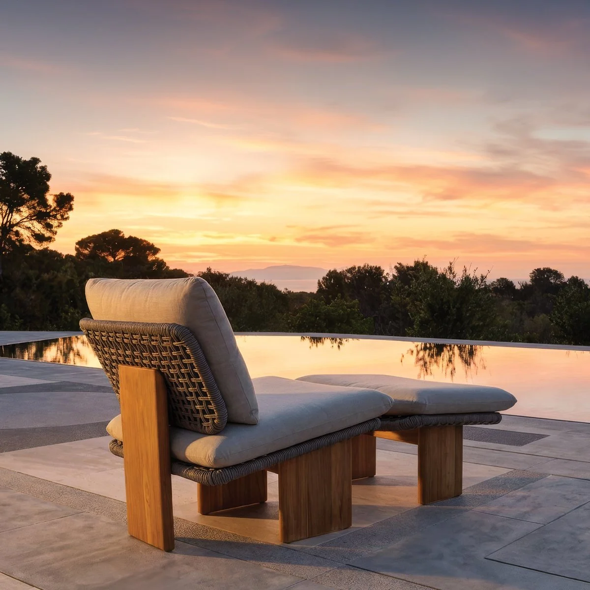 Outdoor patio set with wicker chairs and a table on a tiled terrace, with a tree and scenic view in the background.