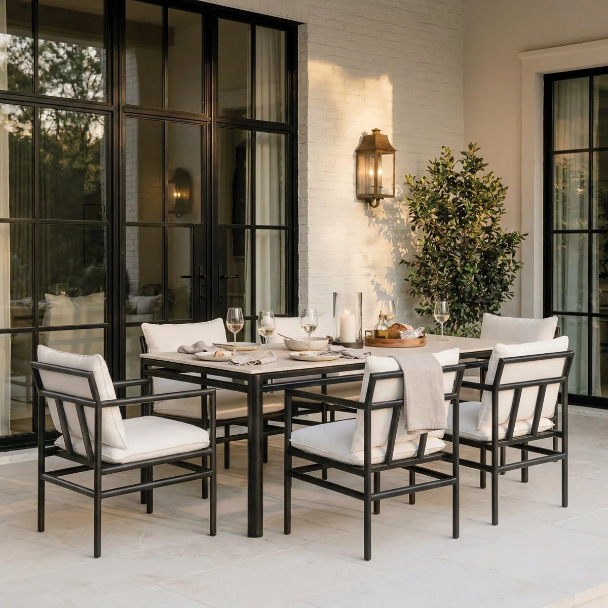 Three outdoor chairs around a fire pit in a backyard with a wooden fence, a large tree, and some small plants.