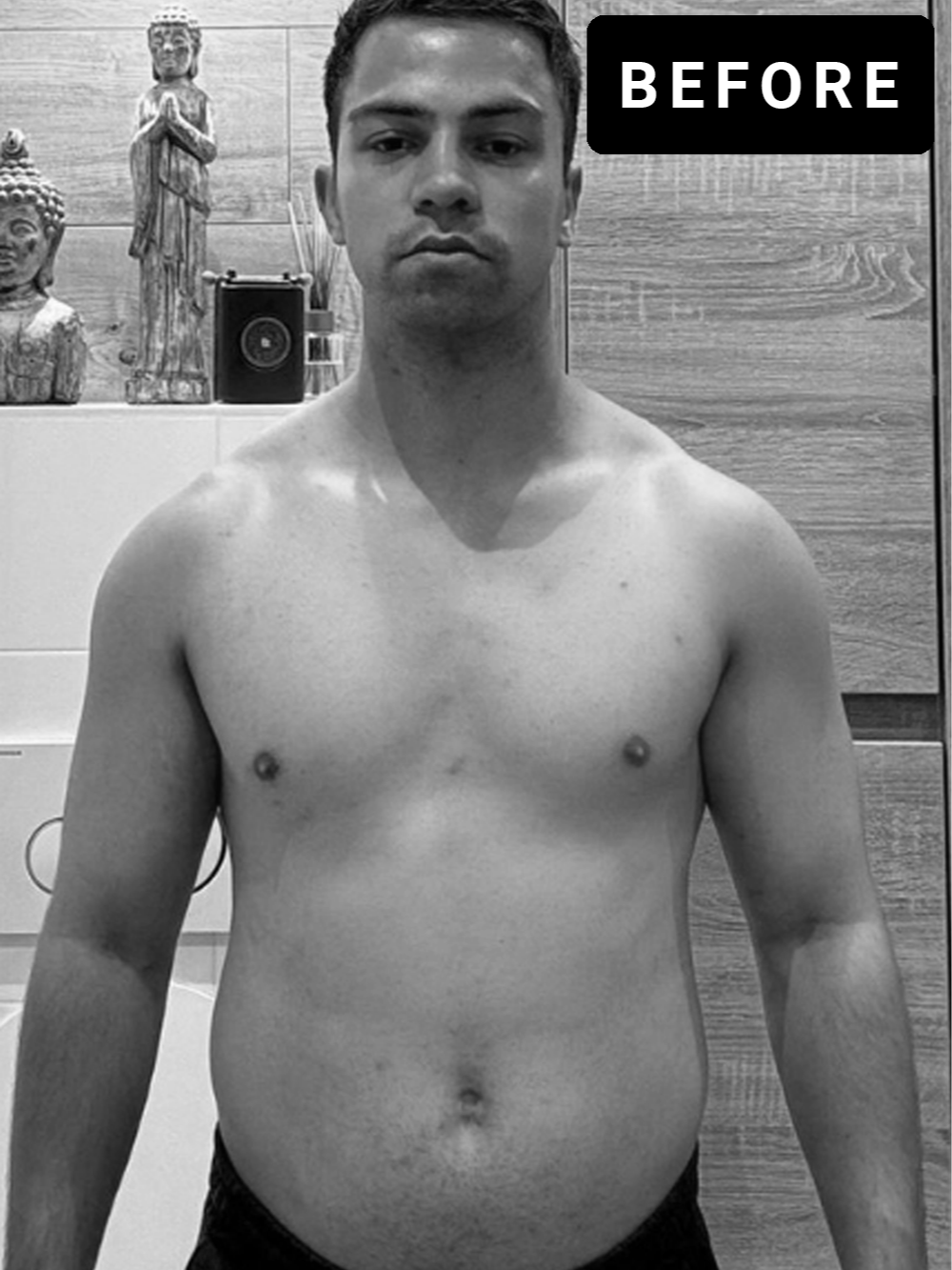 Een shirtloze man staat voor een spiegel in een kamer met houten wandpanelen en decoratieve beelden op een kast op de achtergrond.