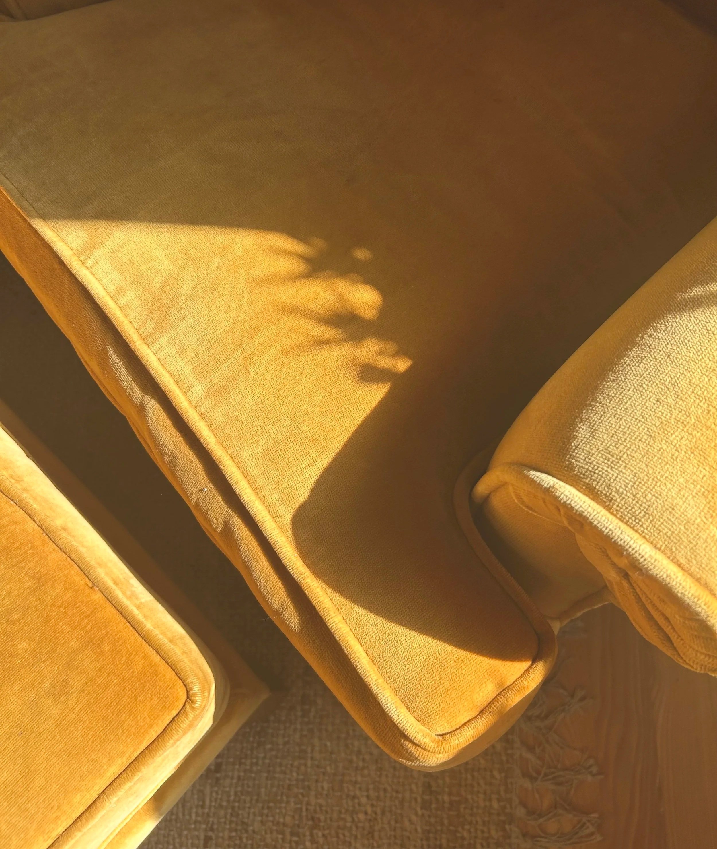 Close-up of a yellow upholstered sofa with sunlight casting a shadow of a plant on it.