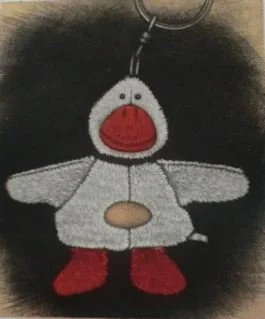The image shows a plush keychain of a cartoon duck with a large red beak, white body, red feet, and small black eyes, hanging from a black surface.