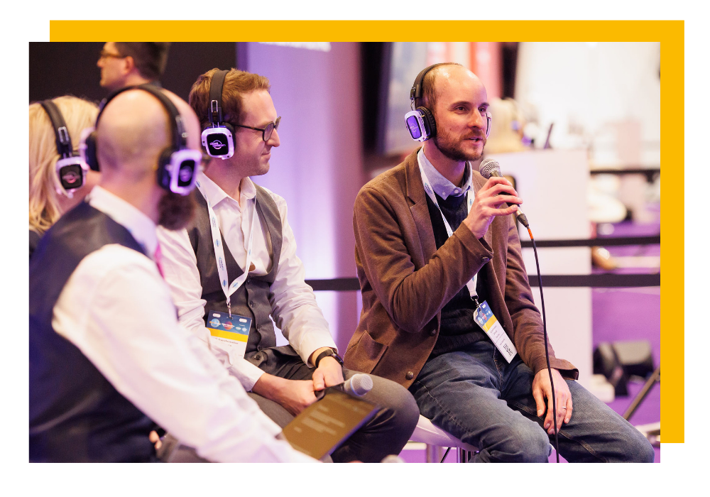 Speakers wearing headphones and holding microphones at the HE Transformation Expo