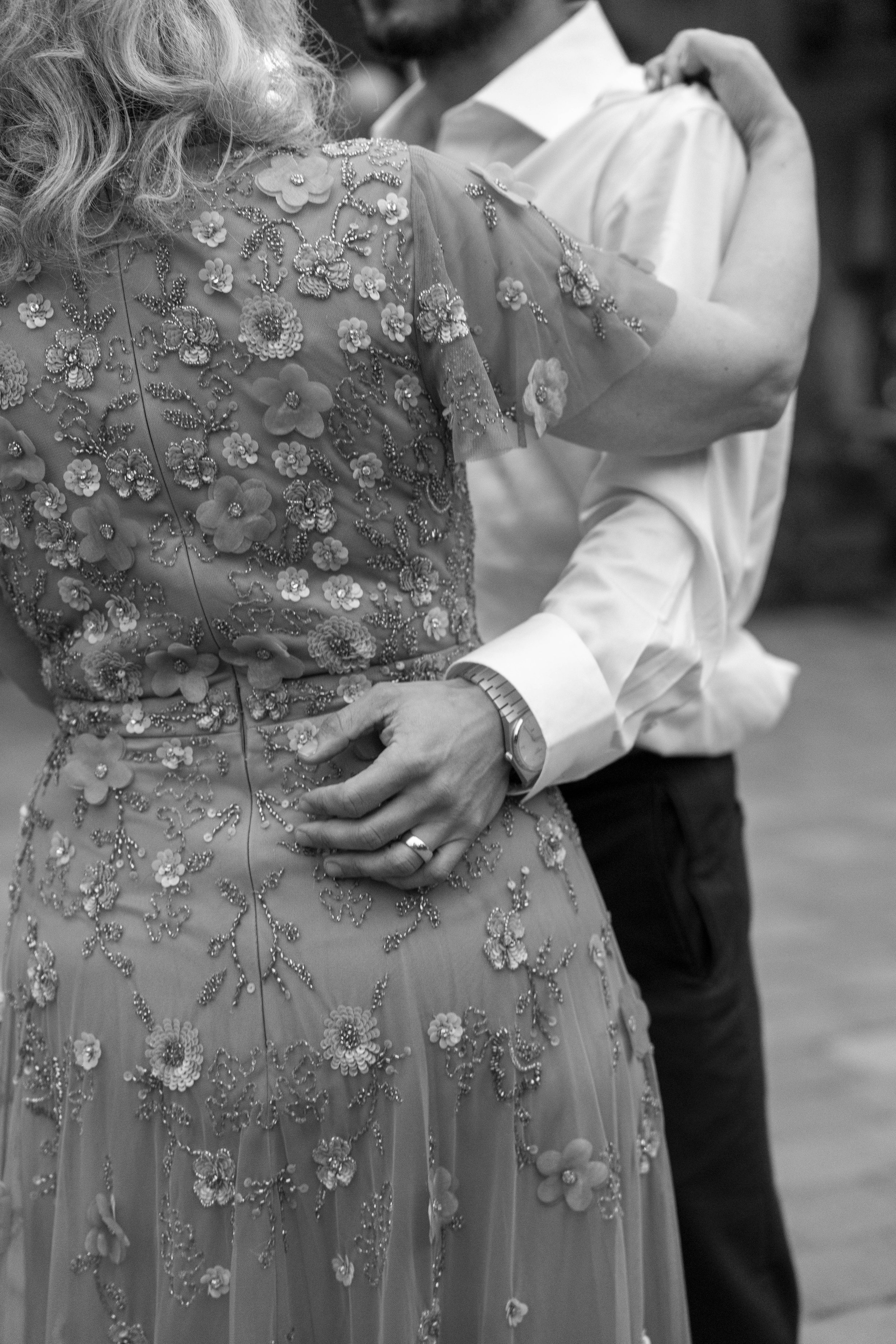 Close-up of a bride in a gown with intricate floral embroidery and beading, and a groom in a white shirt, dancing closely.