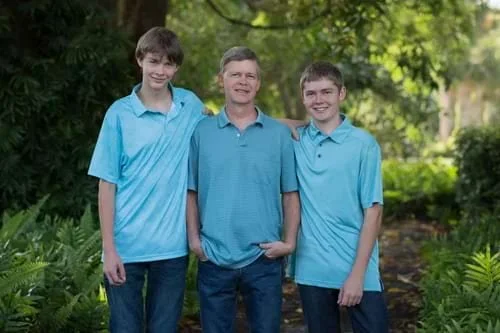 Father standing proudly with his two teenage sons in a green outdoor setting
