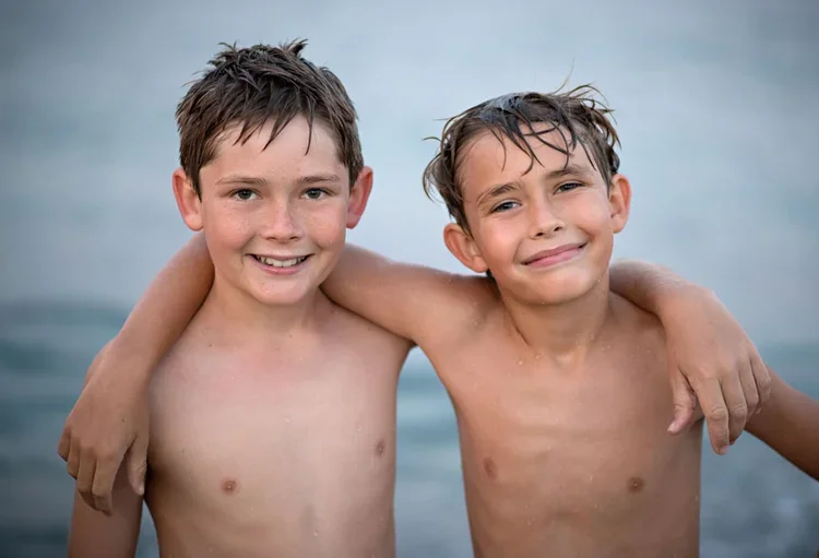 Two boys with wet hair and arms around each other smiling during a beach session