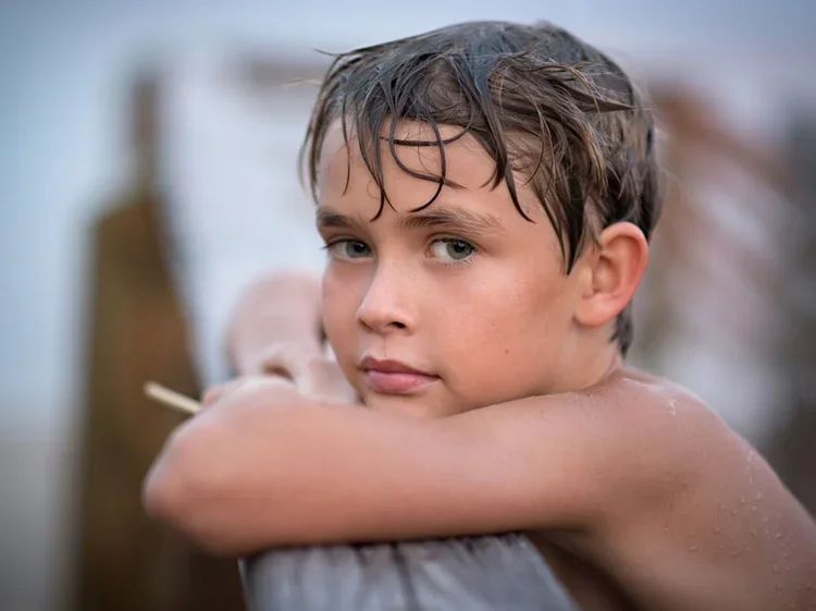 Wet-haired boy leaning on a wooden dock rail during sunset beach portrait in Stuart, Florida