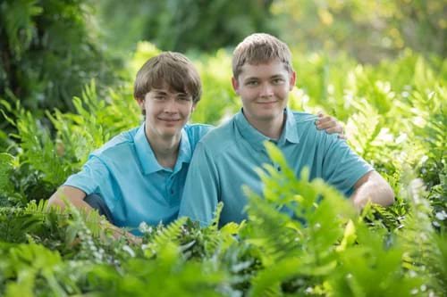 Two teenage brothers smiling in the middle of green ferns during a family portrait session