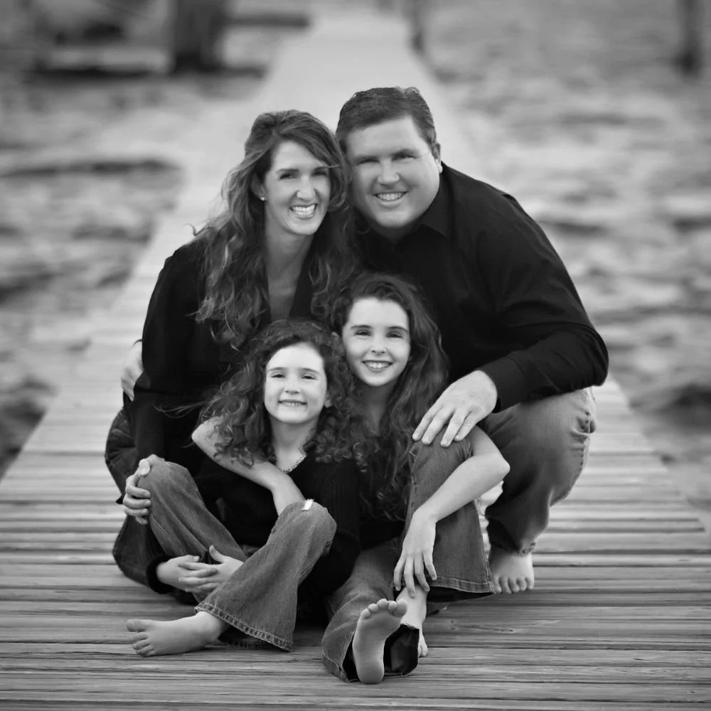Black and white professional portrait of a young family with two small daughters sitting on a wooden pier in Stuart, Florida, by Dultmeier Photography.