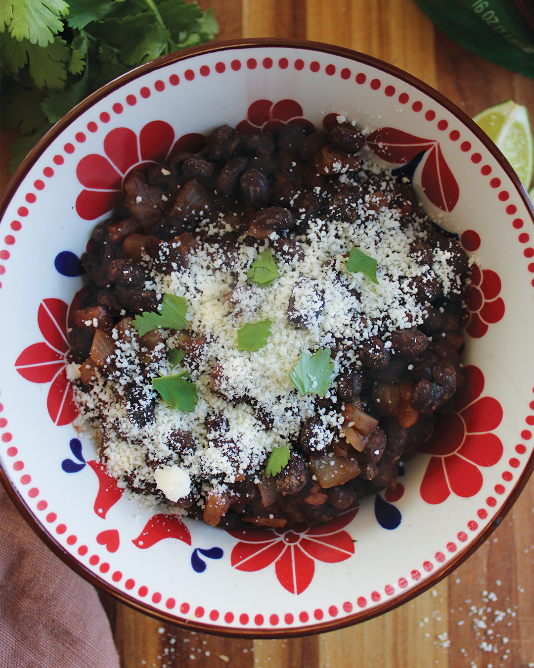 A bowl of black bean soup garnished with crumbled cheese and cilantro leaves, served in a decorated red and white bowl.