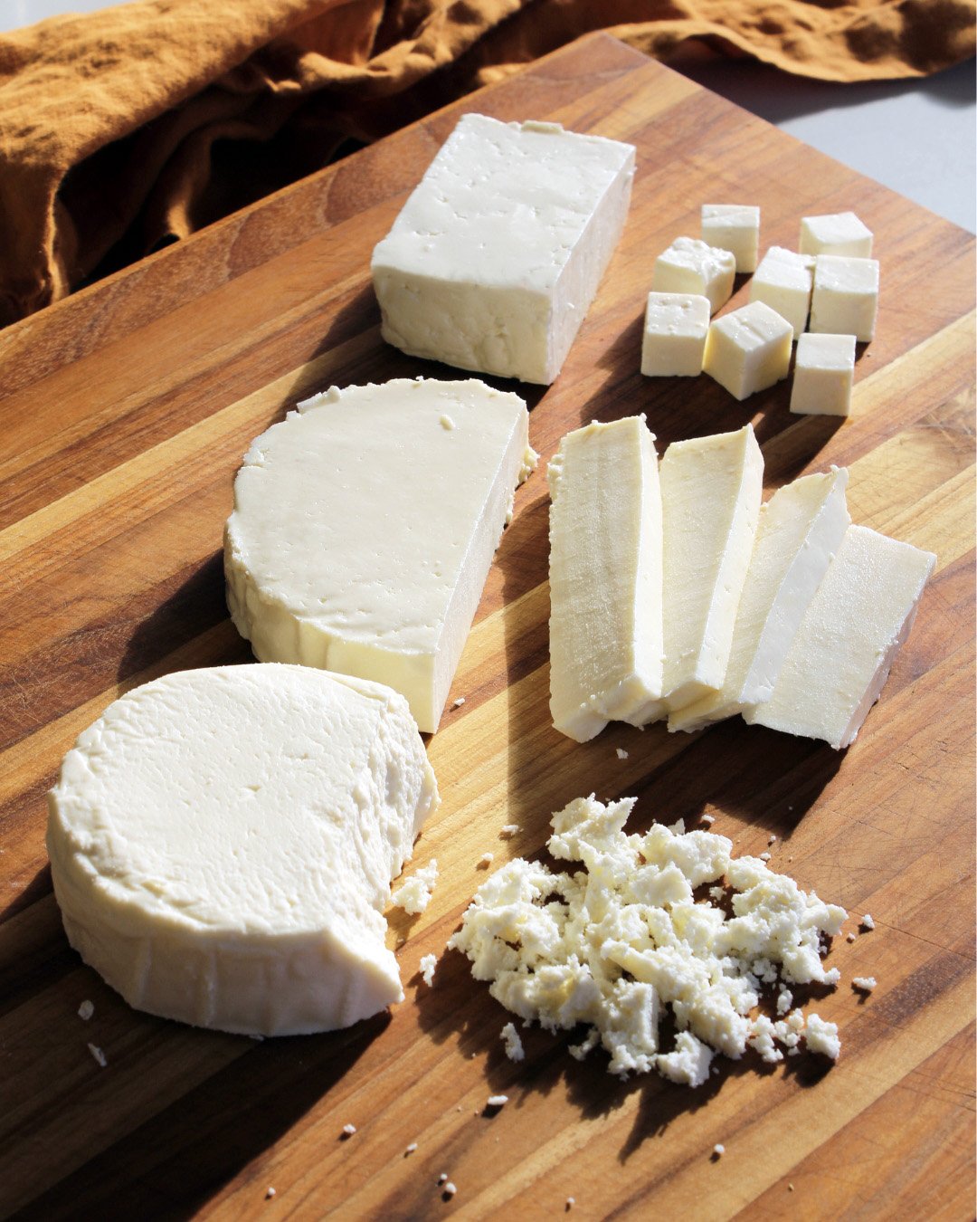 Assortment of white cheeses on a wooden cutting board, including brie, feta, and cubed cheese.