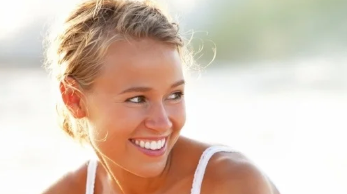 A young woman with blonde hair smiling outdoors during daytime