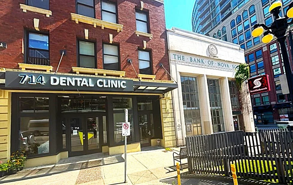 Street view of a building with a dental clinic at 714 and a bank of Nova Scotia to the right, with benches and streetlights in the foreground.