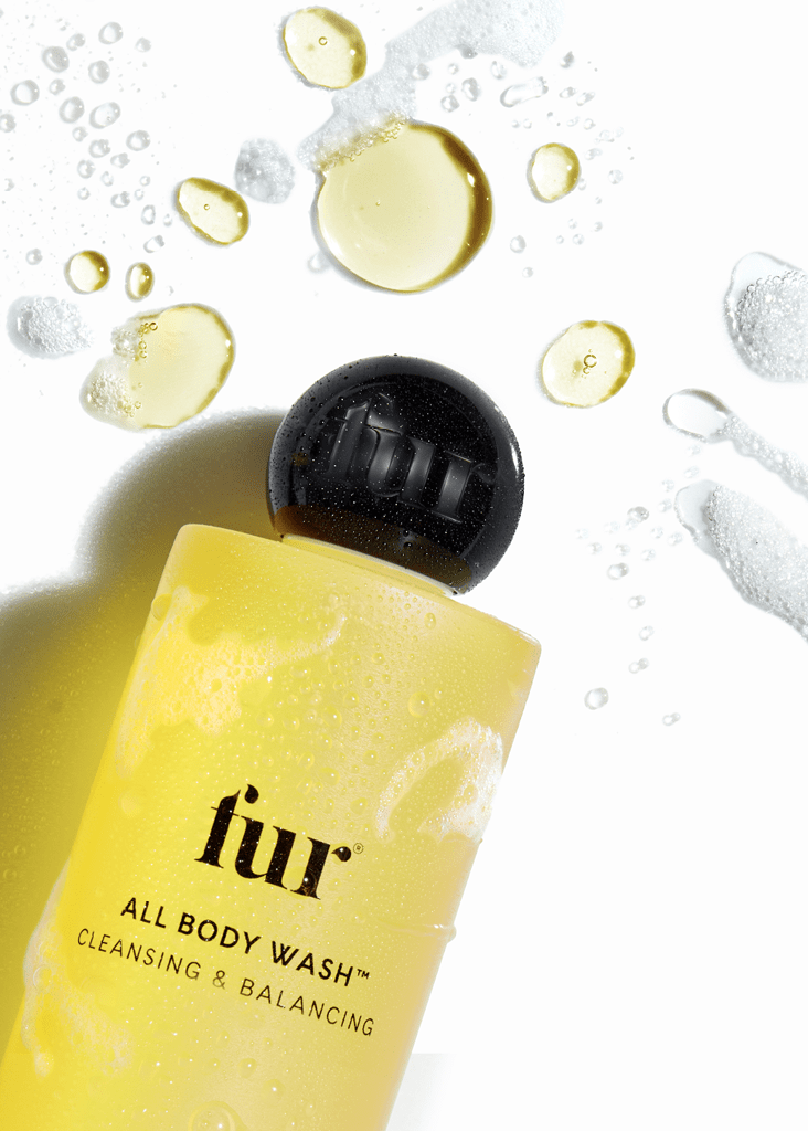 Yellow bottle of LUR all body wash with black cap, surrounded by water droplets and bubbles on a white background.