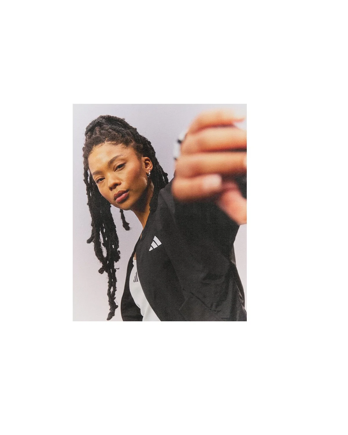 A woman with long dreadlocks taking a selfie with her phone, wearing a black athletic jacket with white accents.