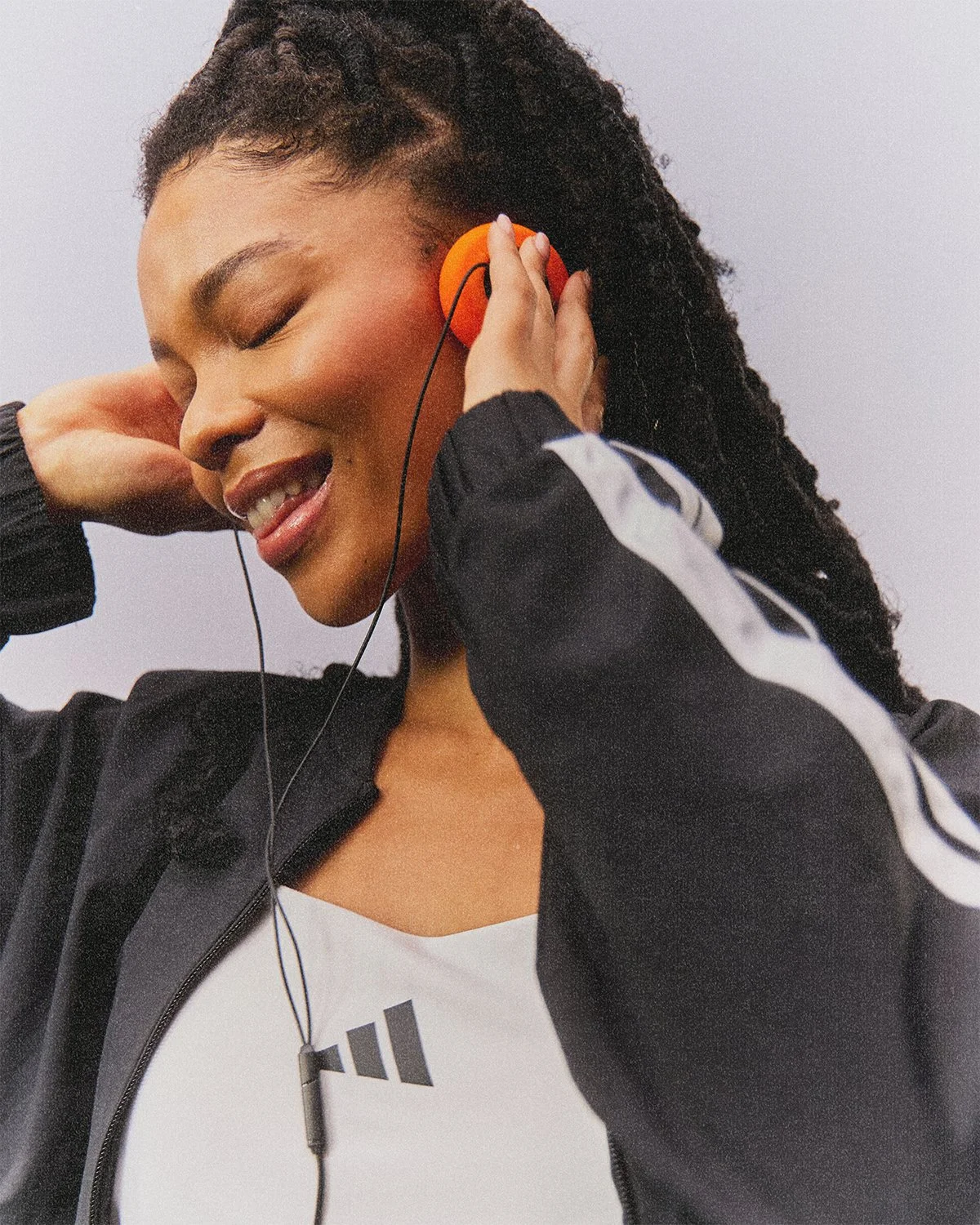 A woman with dreadlocks listening to music with orange headphones, smiling and enjoying herself.