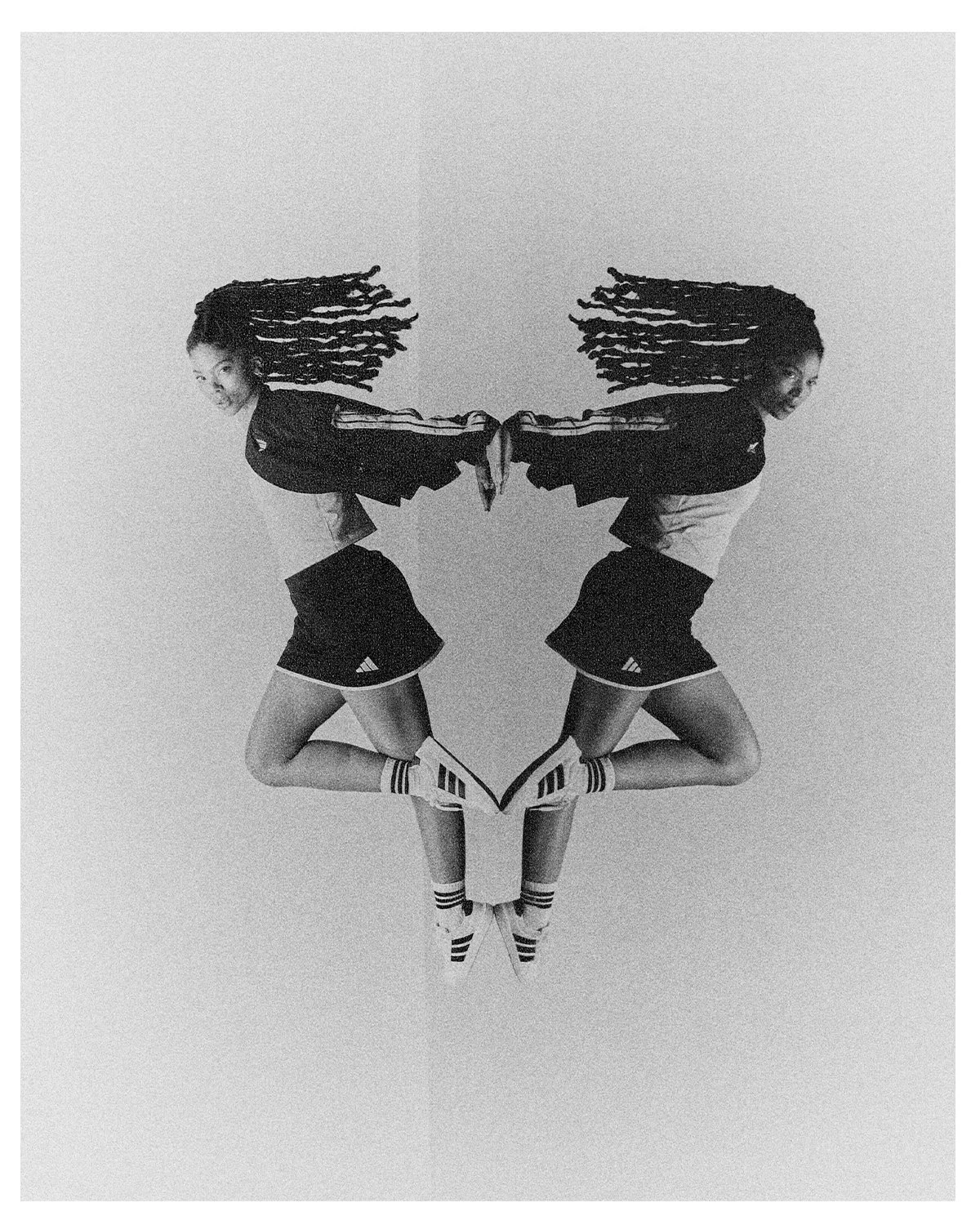 Black and white photo of a woman with voluminous dreadlocks jumping with her reflection creating a mirrored image.