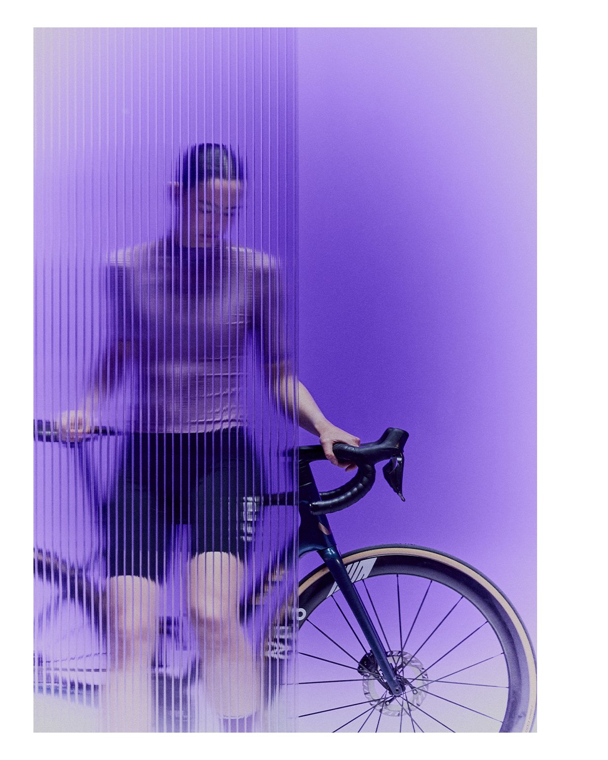 A person standing behind a semi-transparent purple curtain holding a bicycle handlebar, with a purple wall in the background.