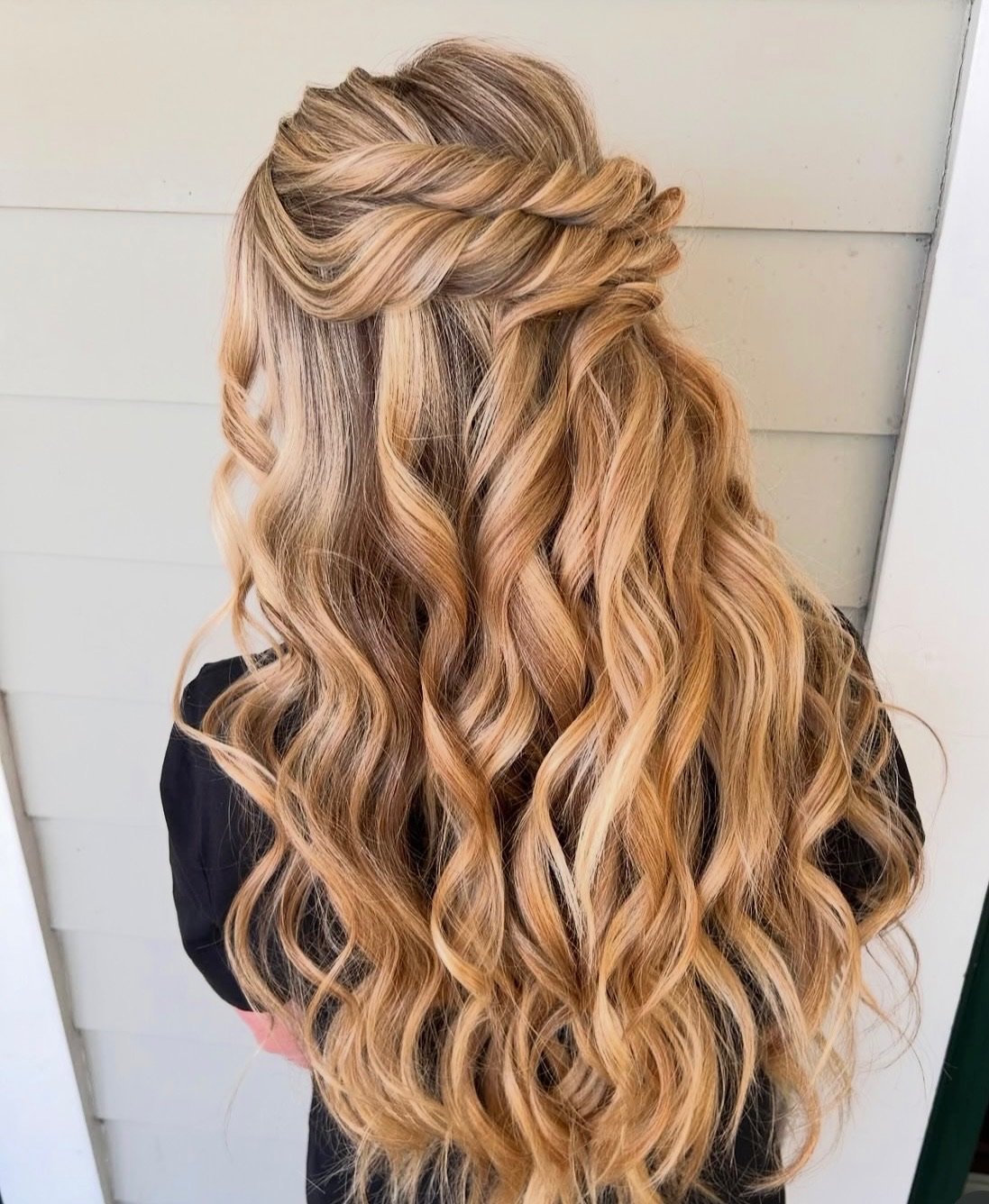 Back view of a person with long, wavy blonde hair styled with a twisted braid at the crown.