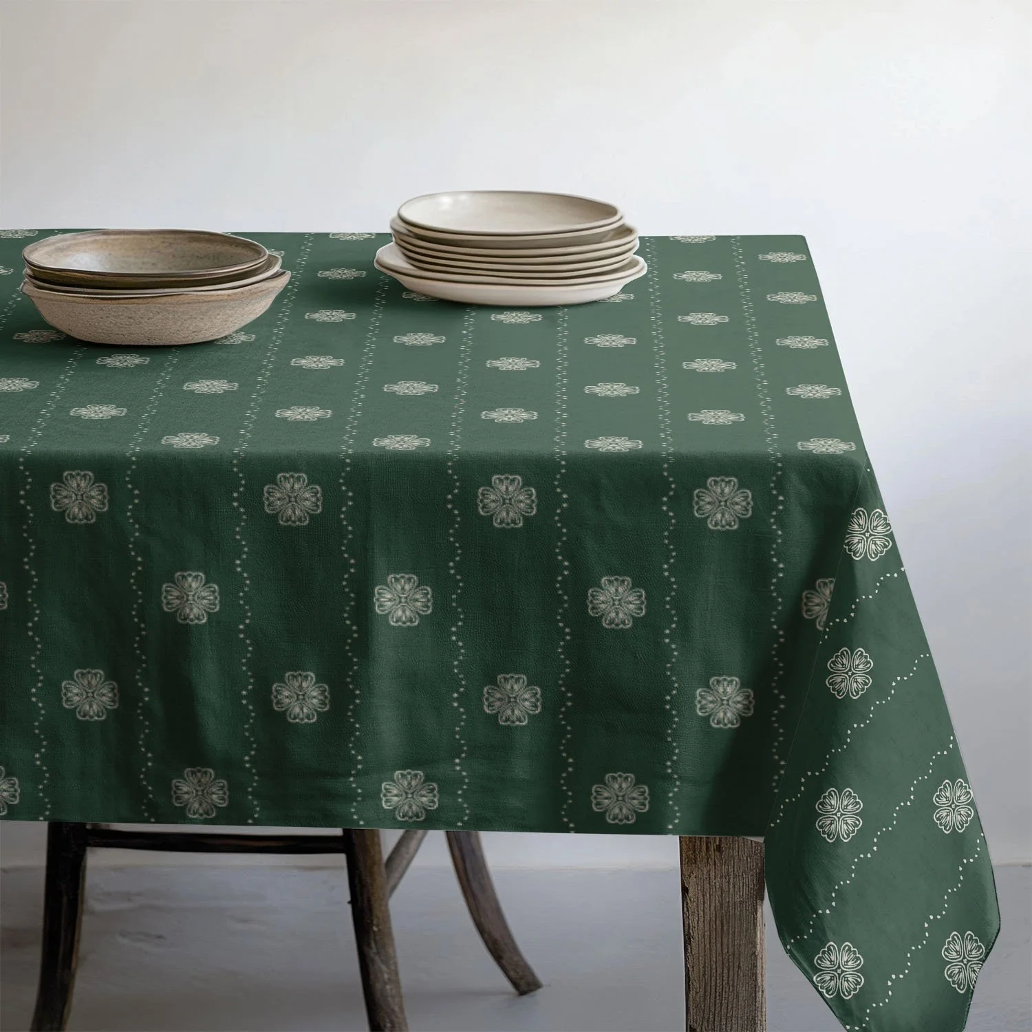 Green floral stripe tablecloth on simple rustic table with stacks of plates and bowls on top.