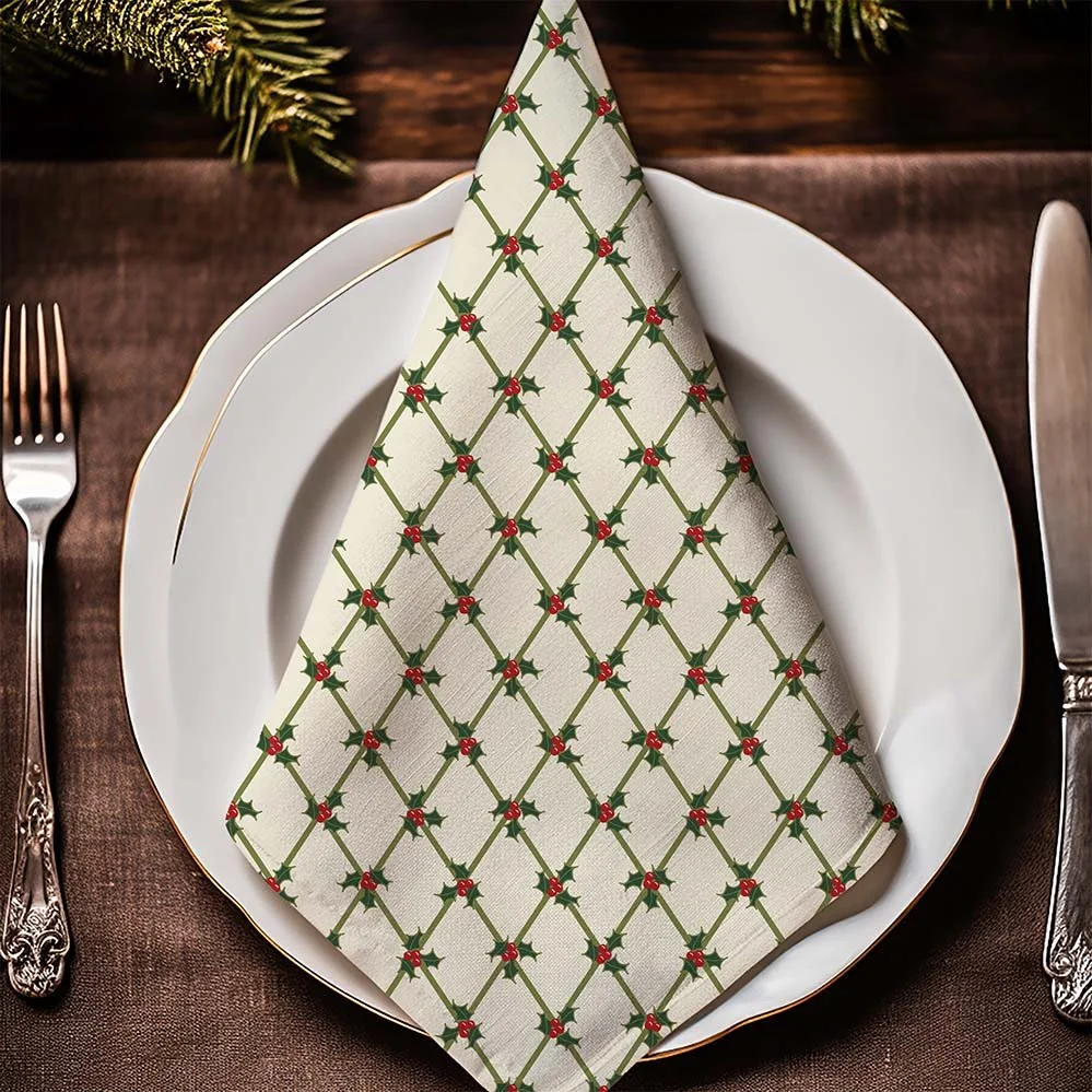 Cream Christmas cloth napkin with a green holly lattice pattern and red berries on a white dinner plate.