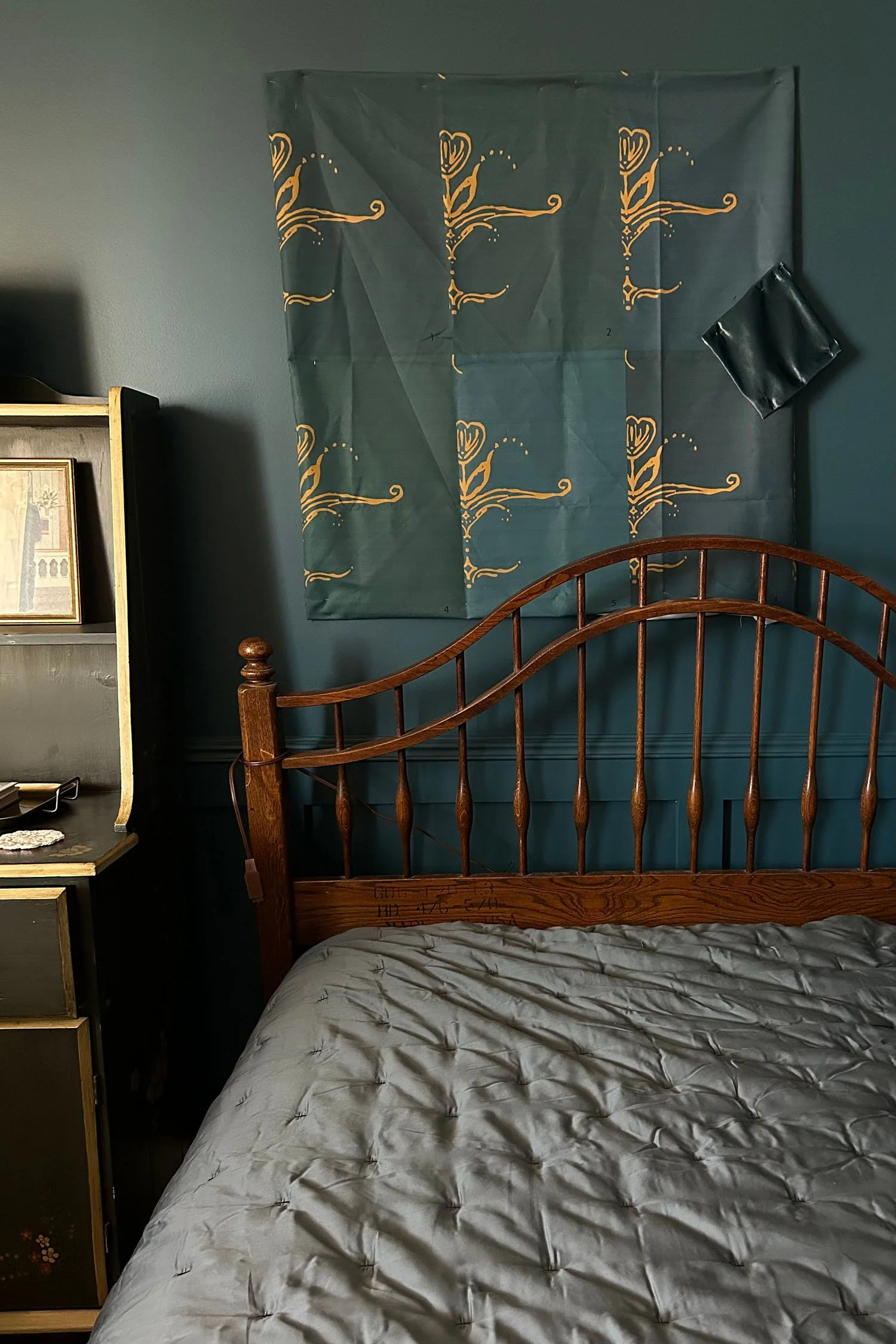 Six teal fabric color samples and a dark velvet swatch pinned above an antique wood bed in a moody teal study.