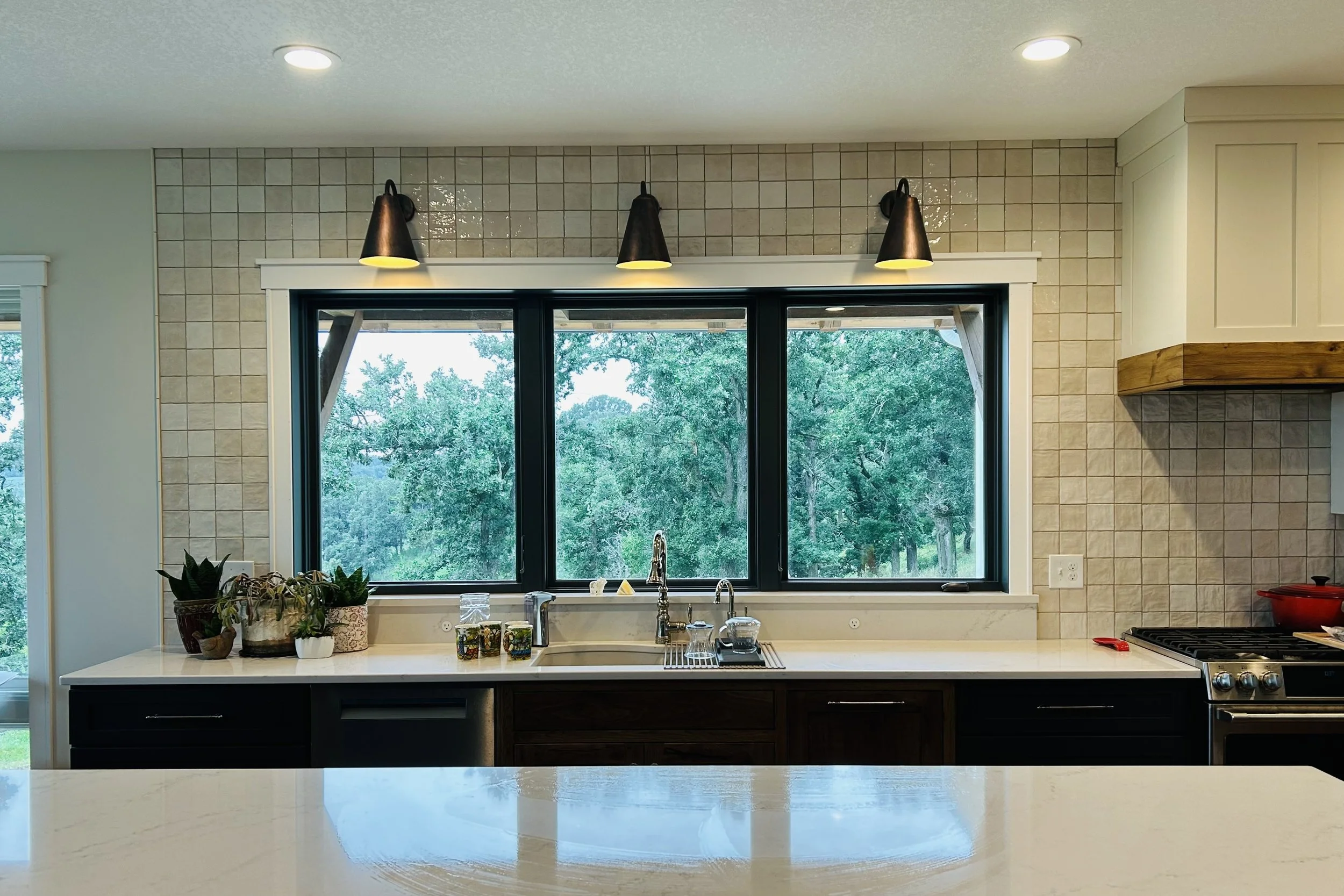 Wide view of a farmhouse kitchen featuring handmade cabinetry, Moroccan sconces above the sink, and countryside views through large windows.