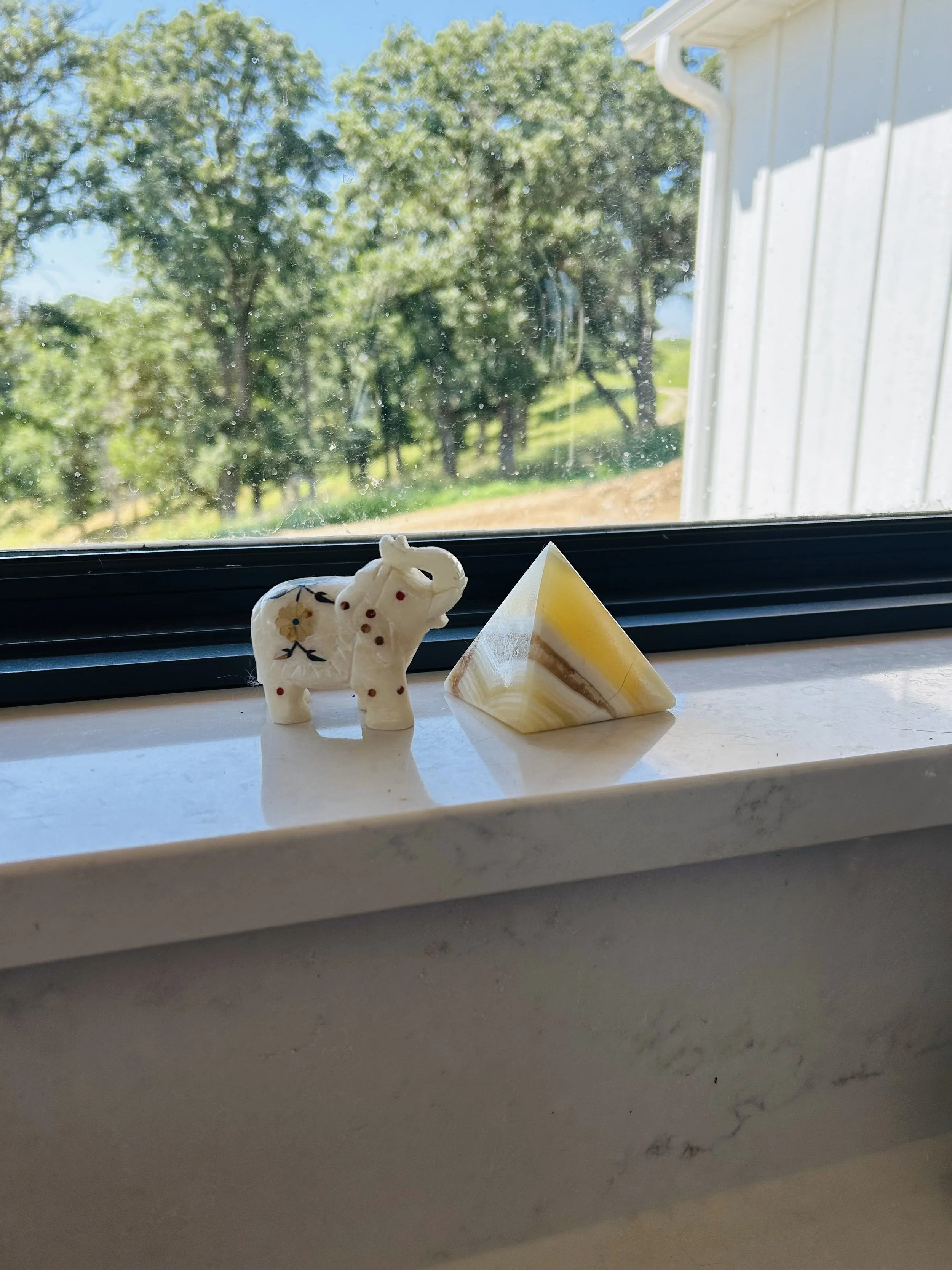 Small marble elephant from India and alabaster pyramid from Egypt displayed on a farmhouse kitchen windowsill.