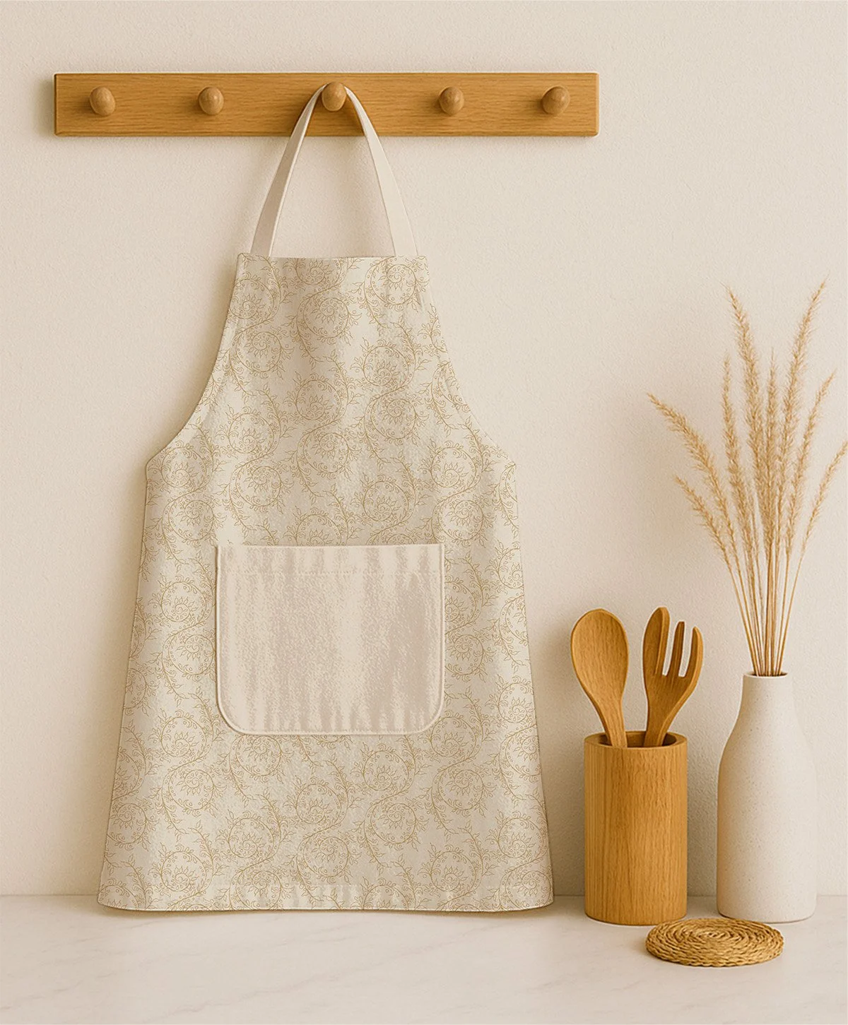 Cream and antique gold apron featuring the hand-drawn Grove Vine botanical pattern, hanging in a warm neutral kitchen setting.
