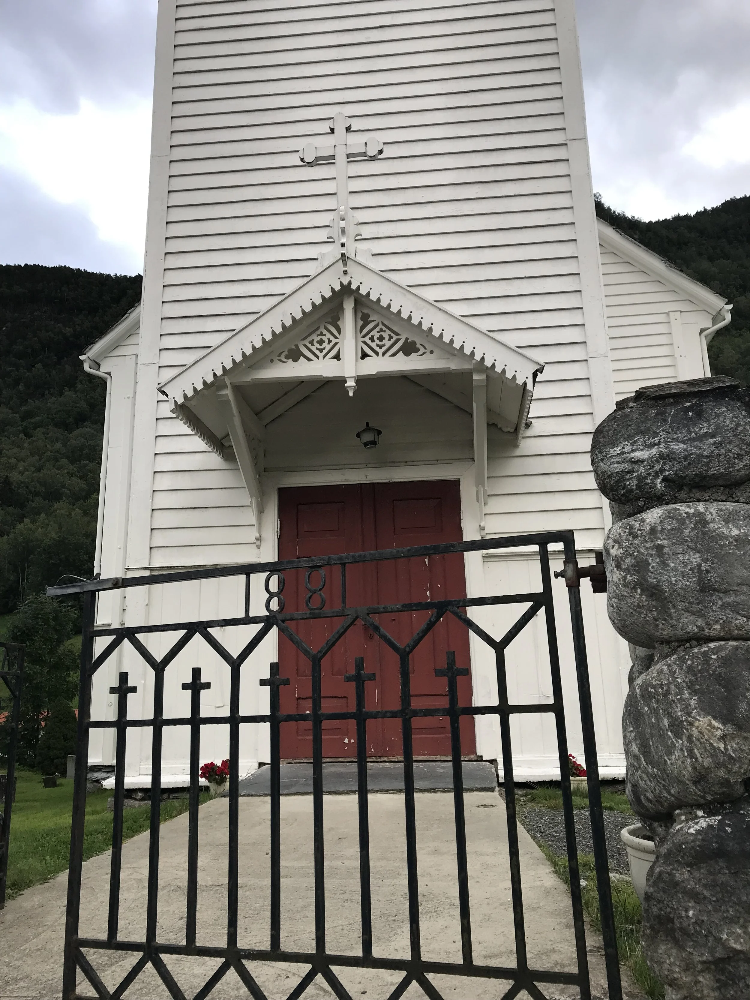 Historic white church in Fresvik, Norway, surrounded by mountains and a small churchyard cemetery.