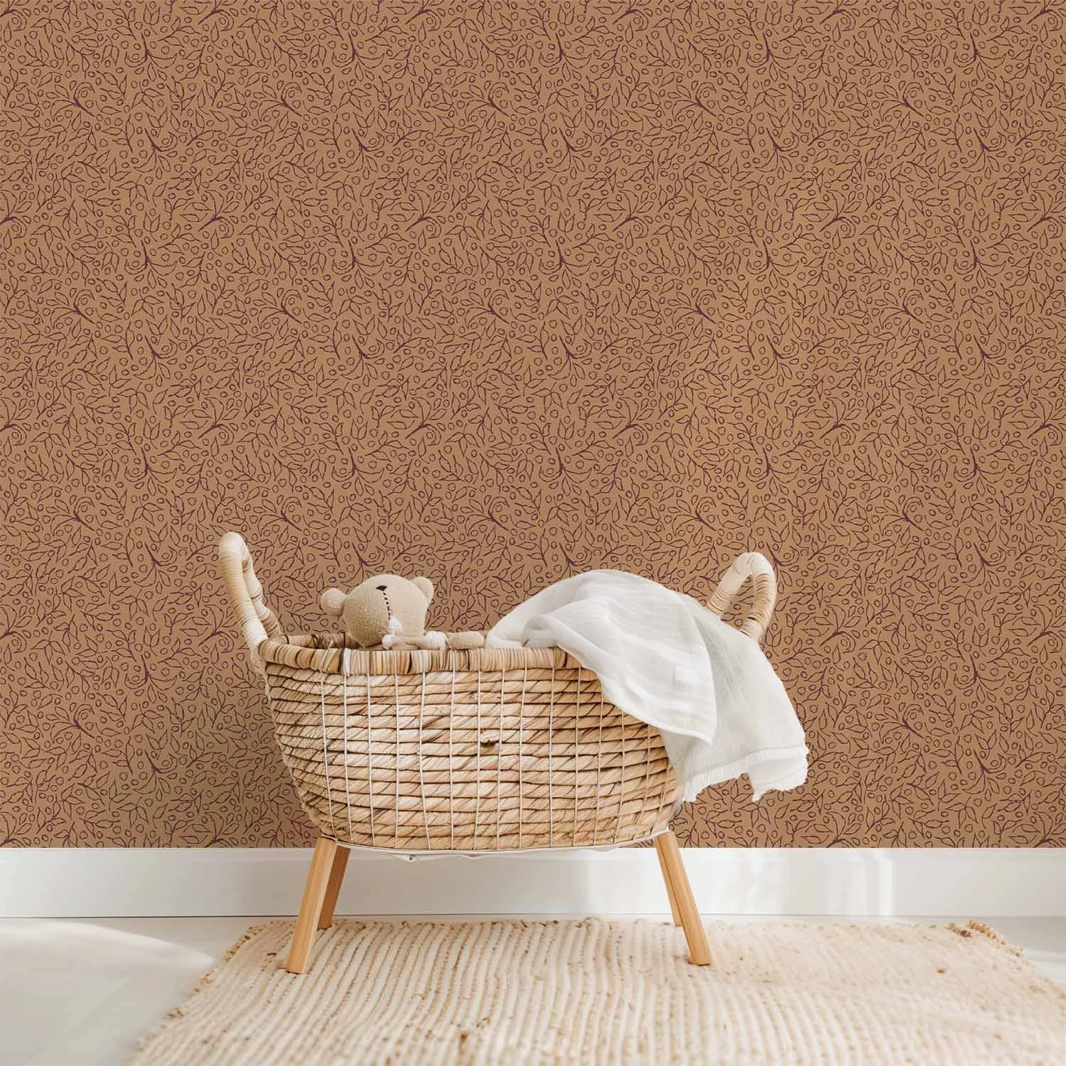 Saddle Cognac Botanical Toss wallpaper with dark botanical linework behind a woven bassinet with a teddy bear and soft ivory blanket.