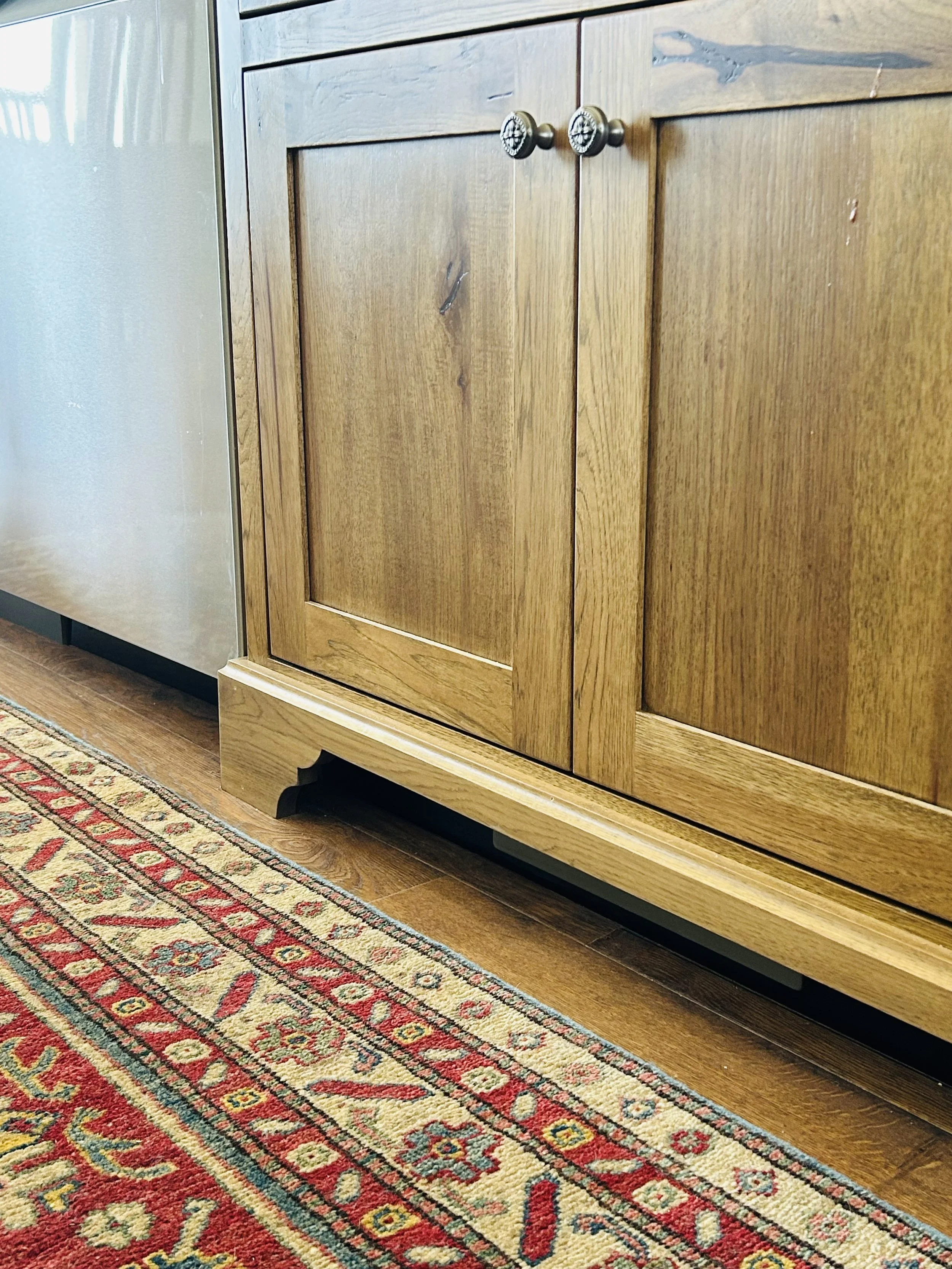 Heritage-inspired furniture-style kitchen cabinetry with shaped feet, stained wood, and a vintage runner rug in a custom farmhouse kitchen.