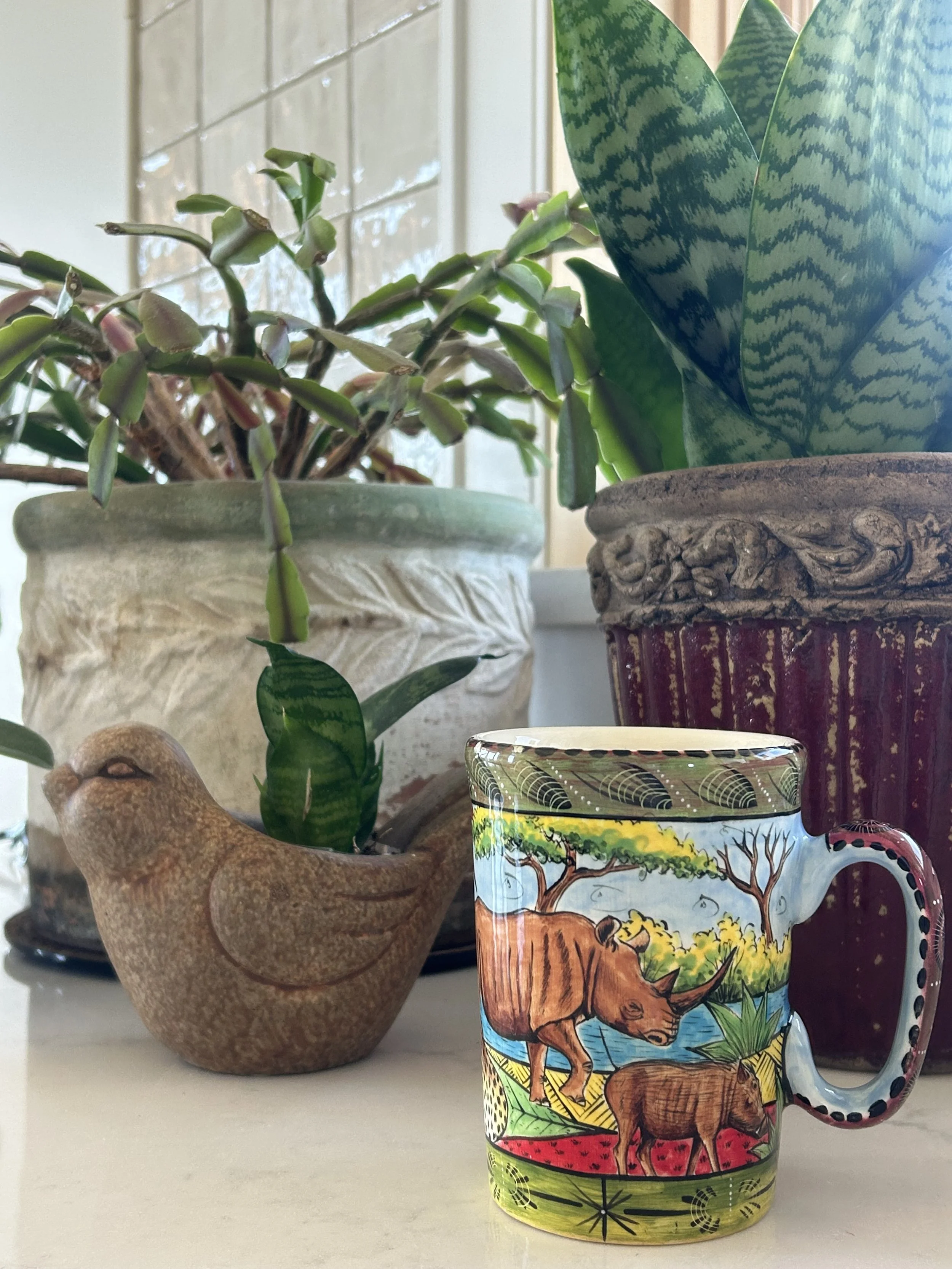 Hand-painted Zimbabwe wildlife mug beside houseplants on a bright kitchen counter.